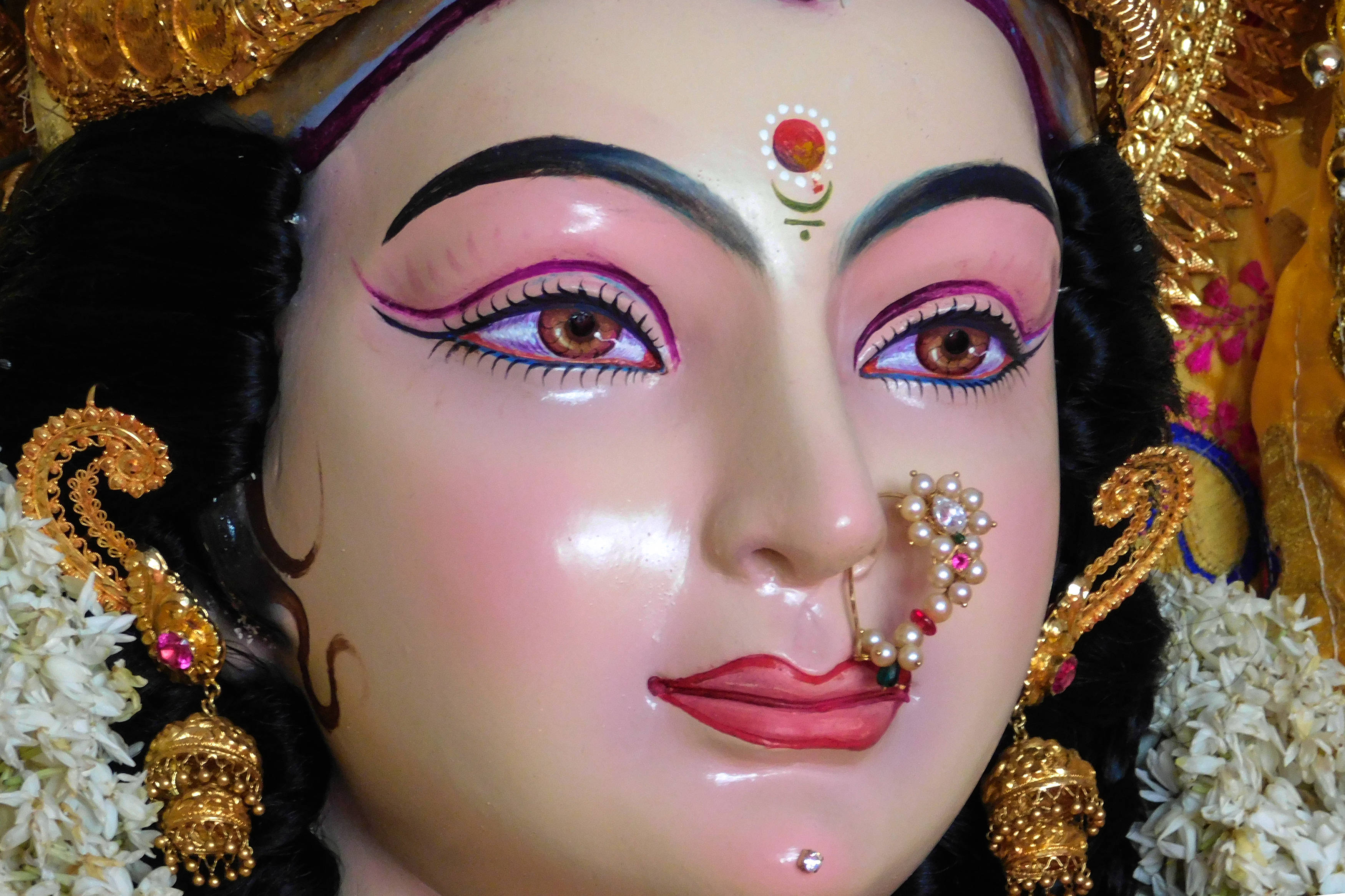 Navratri 桌布 壁紙 — 神聖偶像的特寫，飾有華麗的金飾、粉紅嘴唇和花環，在溫暖燈光下閃耀。