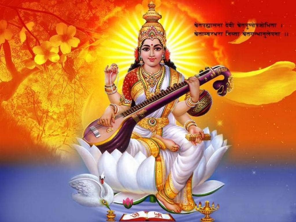 Saraswati Devi 桌布 壁紙 — 神聖的女神薩拉斯瓦蒂優雅地坐在白色蓮花上，手持維納琴，背景是燦爛的橙色和黃色天界。