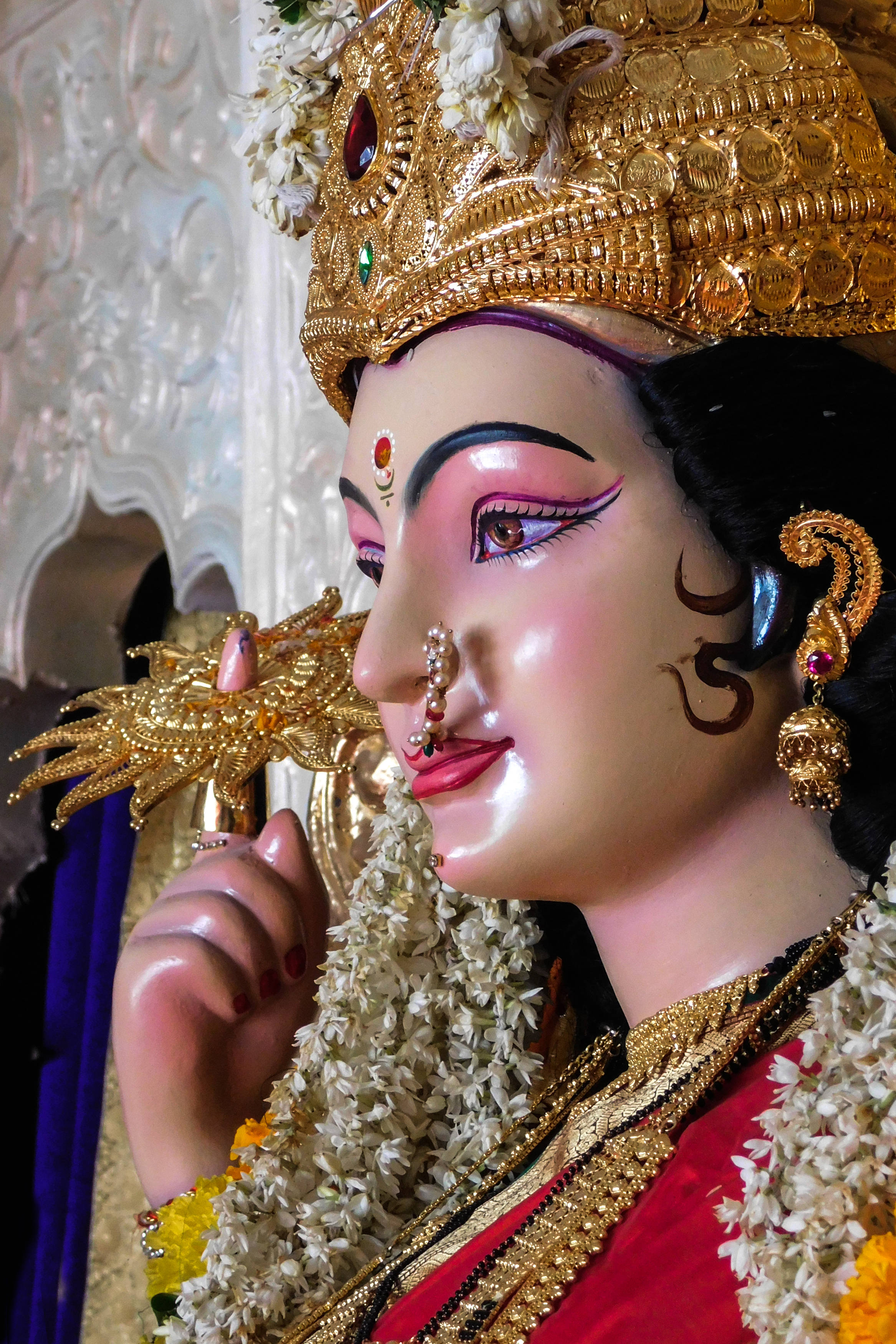 maa durga 桌布 壁紙 — 神聖雕像的特寫，飾有金色王冠珠寶、白色花朵和紅色服飾，手持金色權杖。