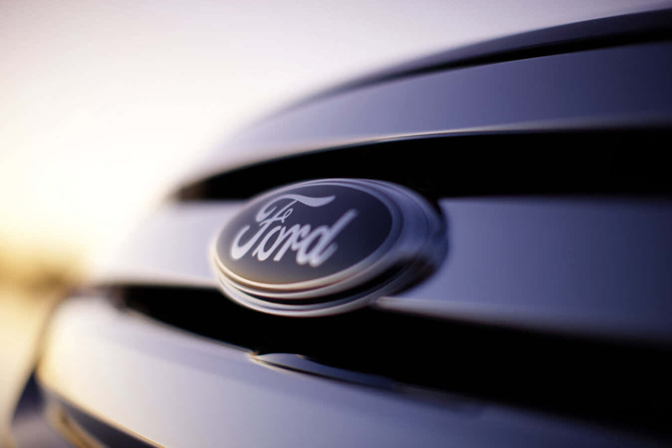 Ford Logo 桌布 壁紙 — 福特標誌特寫，位於時尚的深色汽車格柵上，帶有柔和的金色背光。