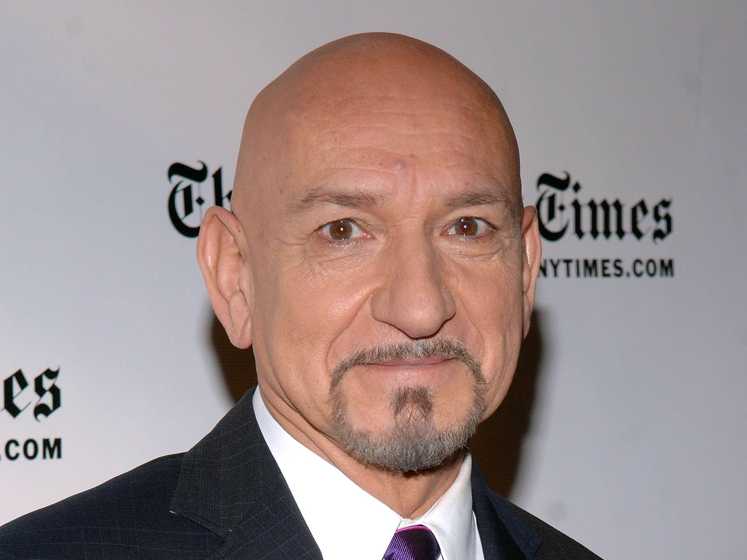 Celebrity 桌布 壁紙 — 禿頭山羊鬍男，身穿深色西裝和紫色領帶，在Times活動背景前。
