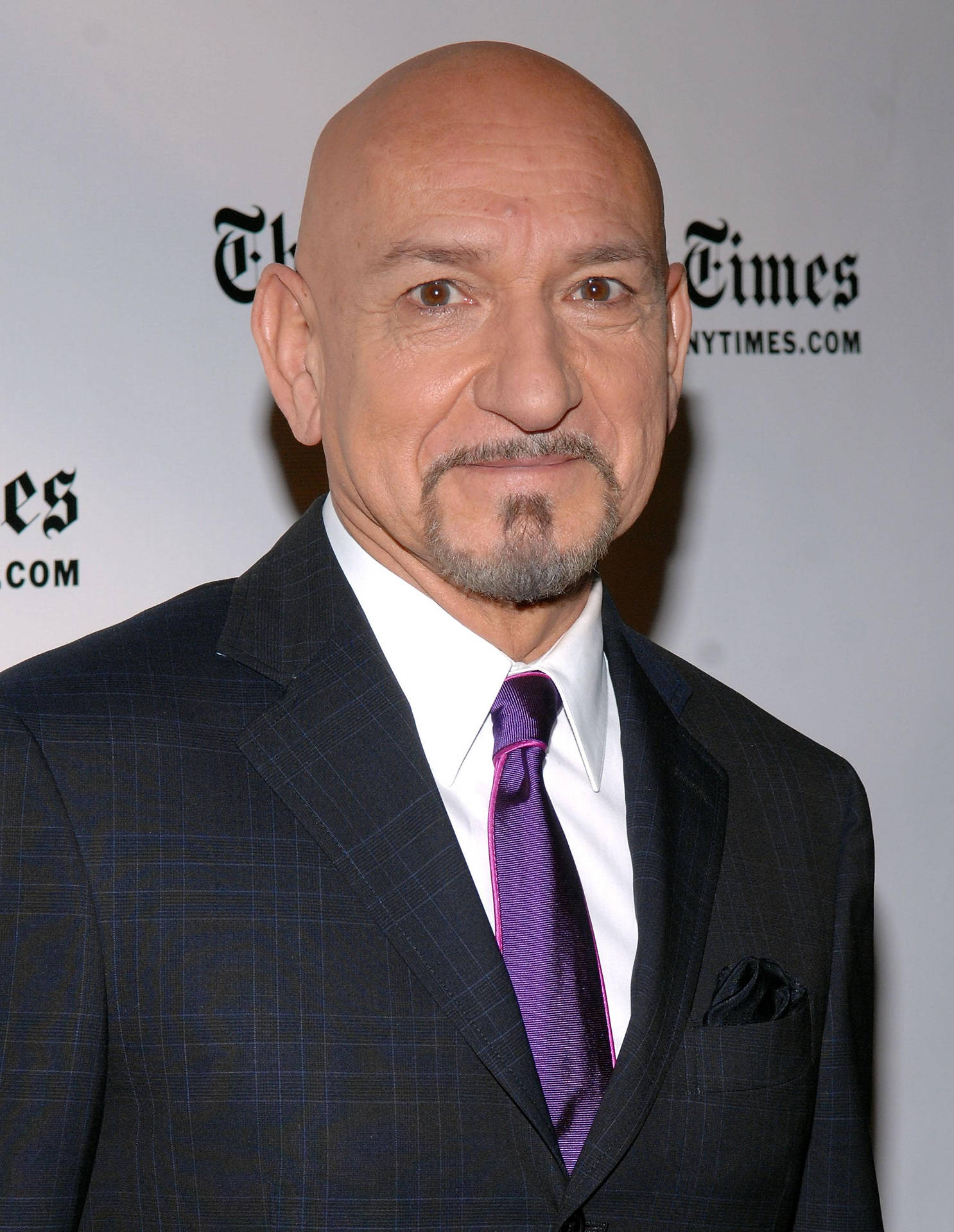 Celebrity 桌布 壁紙 — 禿頭山羊鬍男穿著深色格紋西裝和紫色領帶在Times活動背景前擺姿勢。