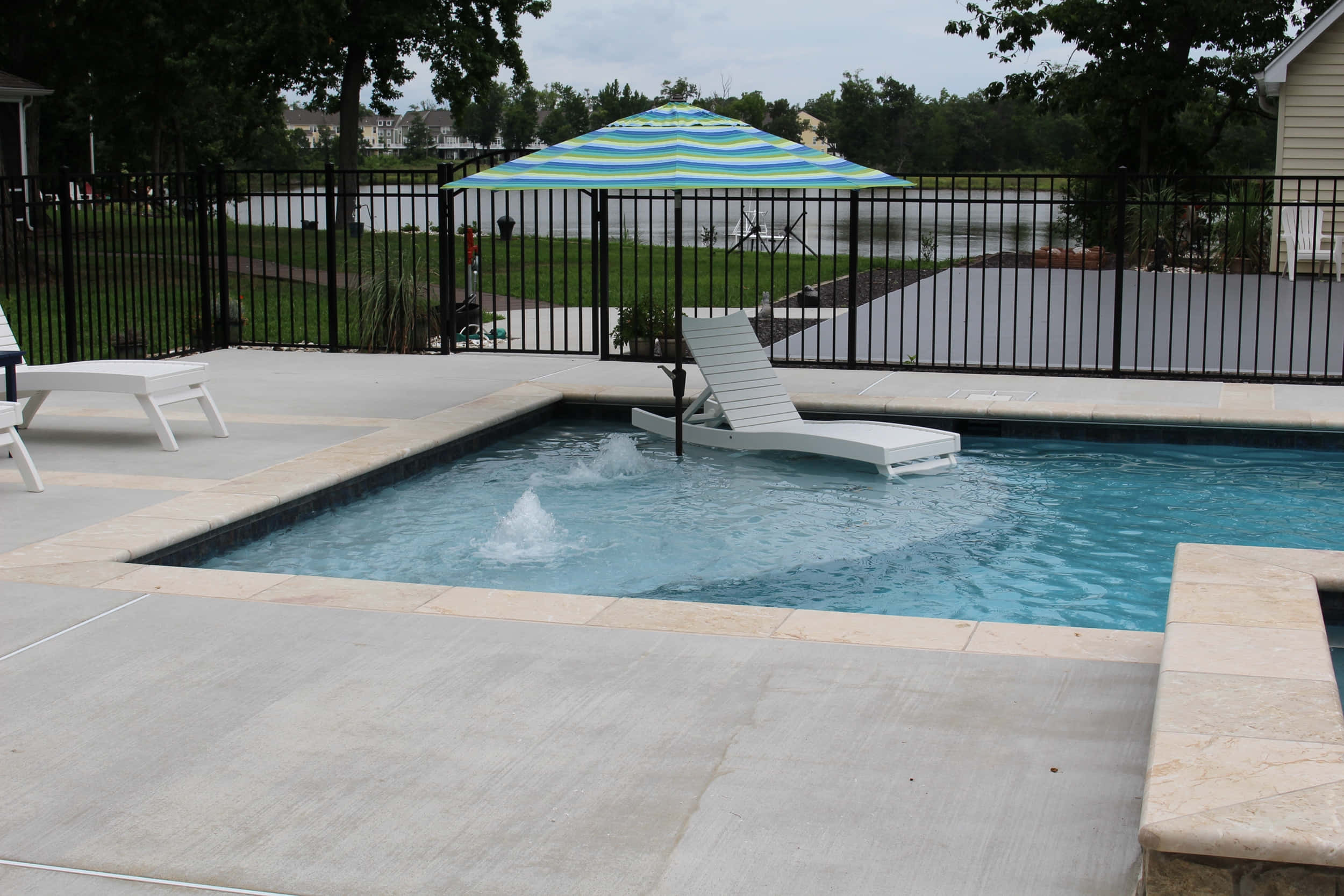 Beach Swimming Pool 桌布 壁紙 — 私人泳池，配備浮動躺椅和條紋遮陽傘，周圍是石質甲板和黑色圍欄，天空多雲。