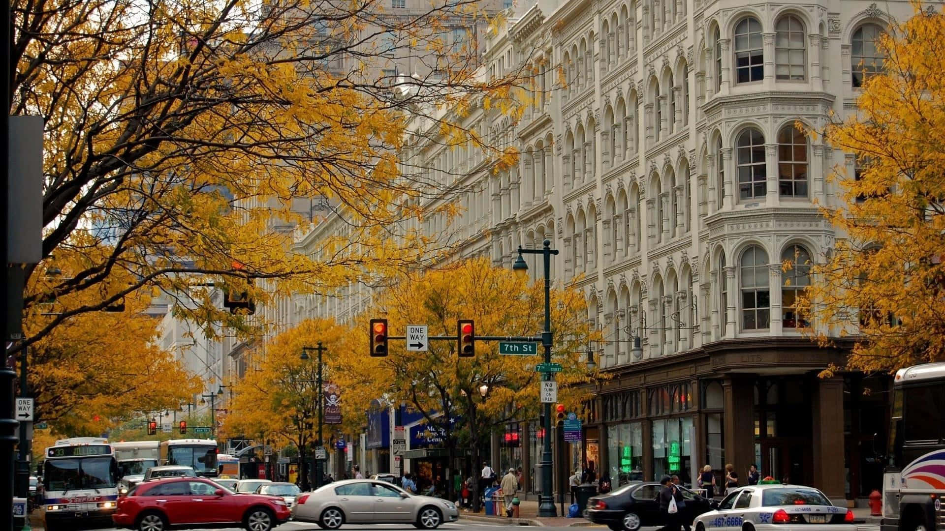 Fall Town 桌布 壁紙 — 秋葉金燦燦地燃燒在繁華的城市街道上，街道兩旁是歷史建築和行駛的車輛。