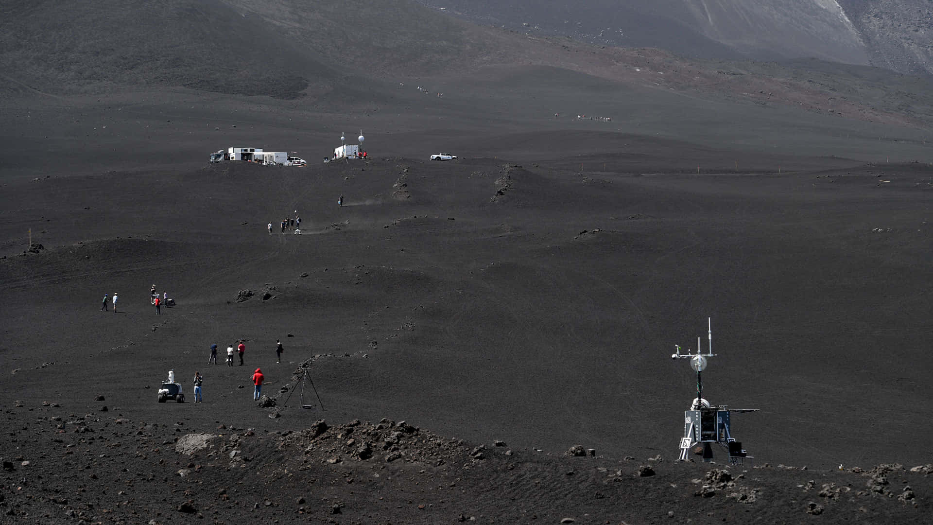 機器人 桌布 壁紙 — 科學家探索廣闊的黑色火山地貌，研究車輛和設備散落在崎嶇的地形上。