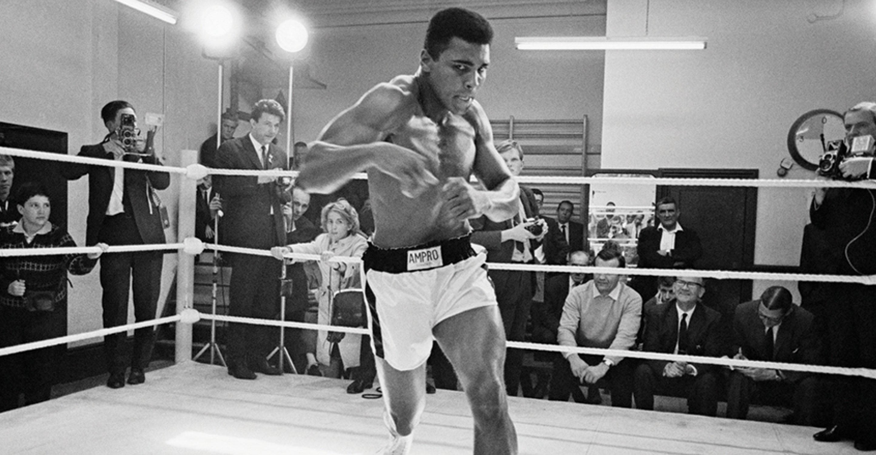 Muhammad 桌布 壁紙 — 穆罕默德·阿里在拳擊擂台上揮拳，周圍有攝影師和觀眾，黑白照片。