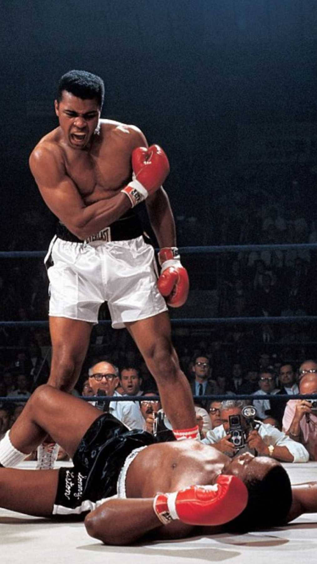 Cool Boxing 桌布 壁紙 — 穆罕默德·阿里在燈火通明的拳擊台上，站在倒下的對手之上，背景是喧囂的人群。