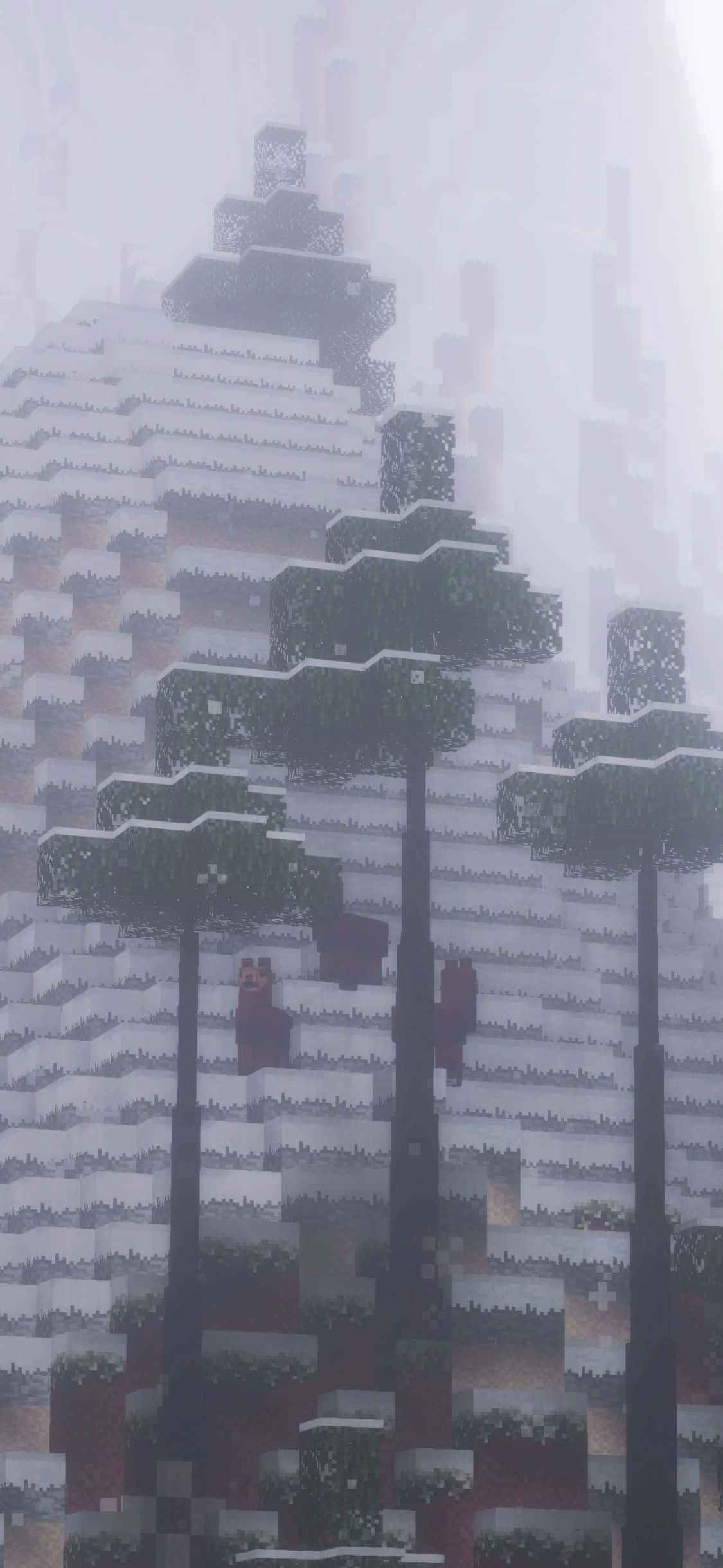 iPhone Xs Minecraft 桌布 壁紙 — 積雪的像素化樹木矗立在霧氣瀰漫的Minecraft冬季場景中一座高聳的塊狀山脈前。