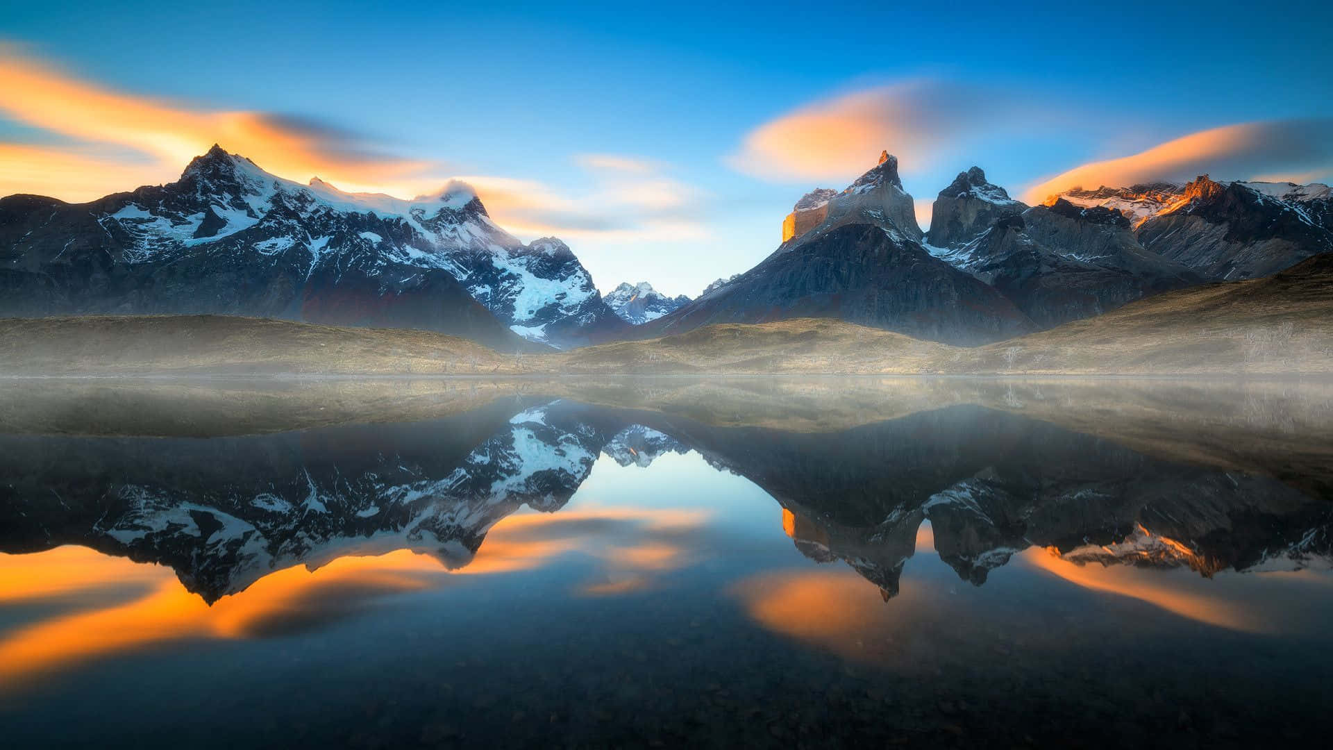 Patagonia 桌布 壁紙 — 積雪的山峰倒映在霧氣瀰漫的湖中，金色雲彩劃過暮色天空。
