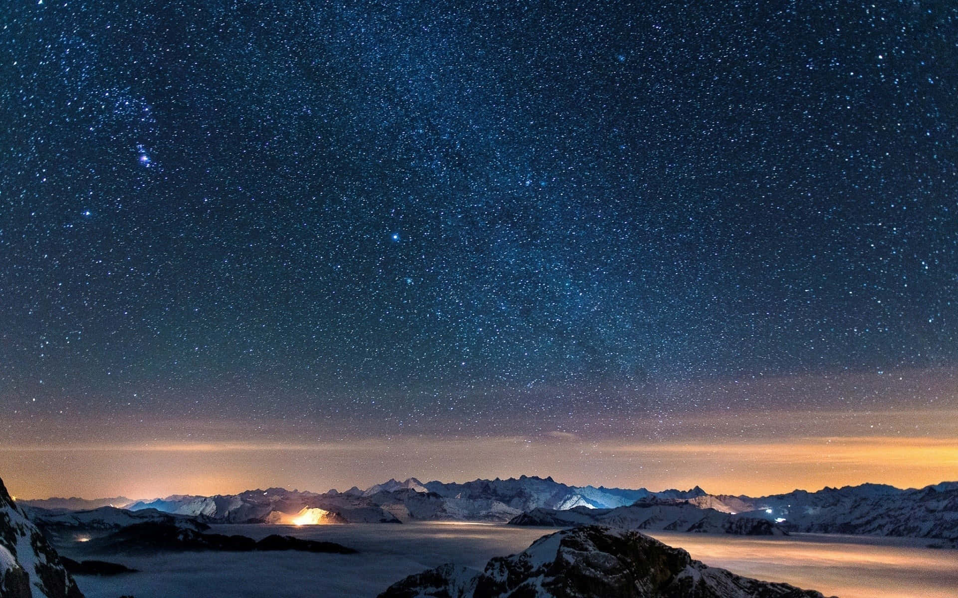 Starry Night Sky 桌布 壁紙 — 積雪的山峰刺穿夜空中的星爆天空，下方是發光的山谷。