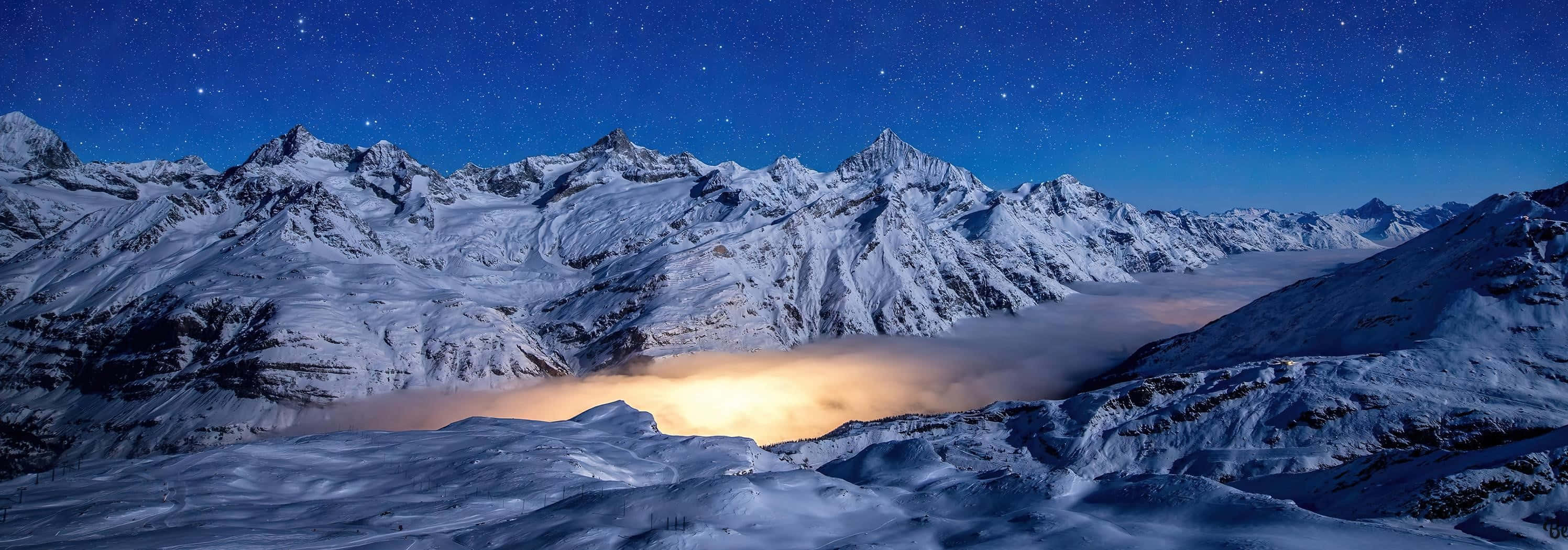 山景 桌布 壁紙 — 積雪的山峰刺穿繁星點點的夜空，下方是發光的雲海。