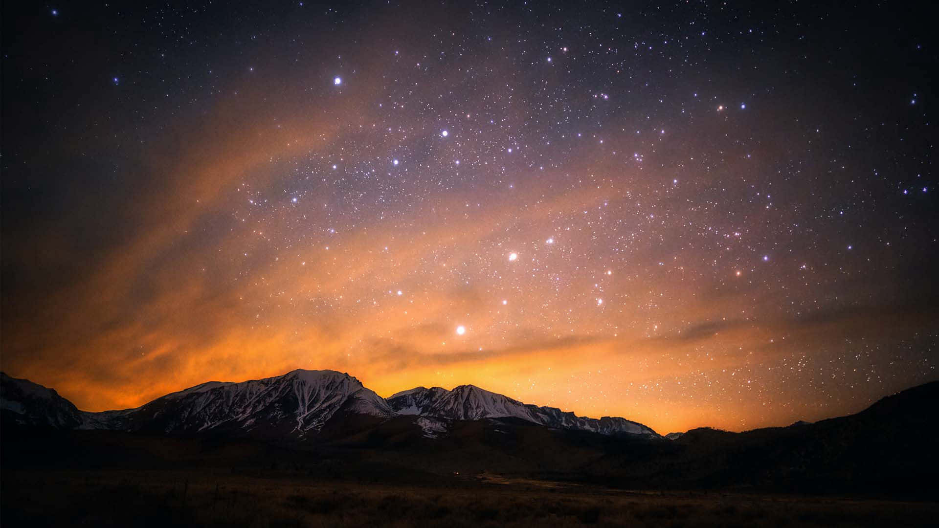 Stars 桌布 壁紙 — 積雪的山峰剪影，在充滿活力的星空夜空下，閃耀著橙色極光雲。