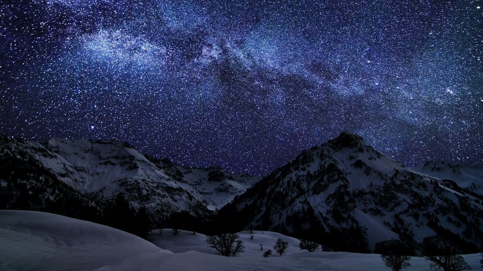 1600x900 桌布 壁紙 — 積雪的山峰在令人嘆為觀止的星空下聳立，銀河散發著鮮豔的藍色和紫色光芒。