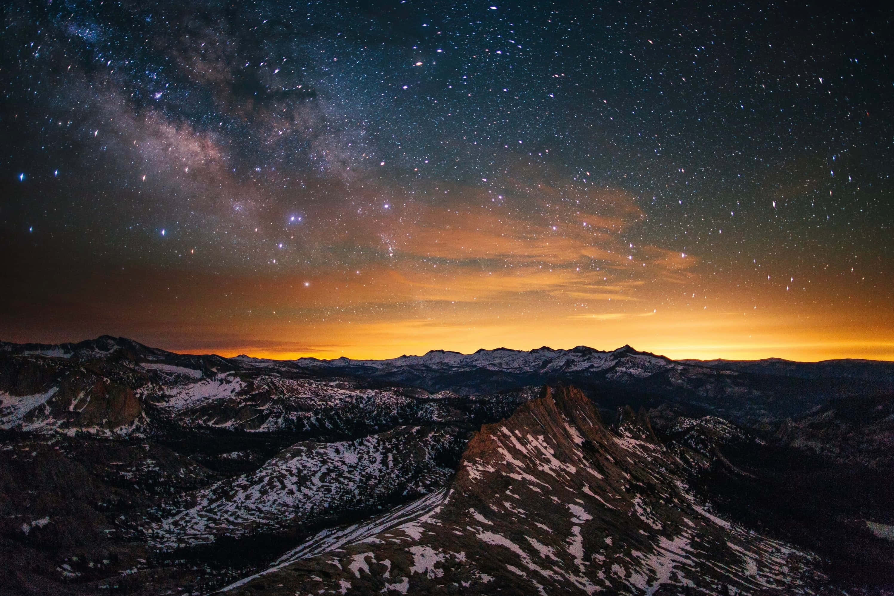 Starry 桌布 壁紙 — 積雪的山峰在佈滿銀河和發光橙色雲彩的鮮豔暮色天空下聳立。