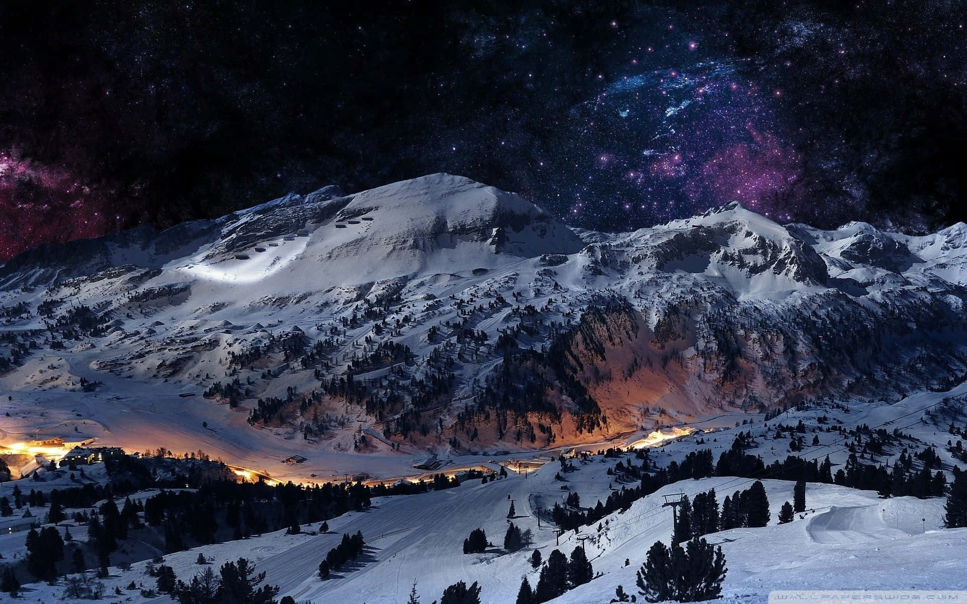 High Resolution Snow 桌布 壁紙 — 積雪的山峰在充滿活力的星空下閃耀，伴隨著紫色星雲和遠處的村莊燈光。
