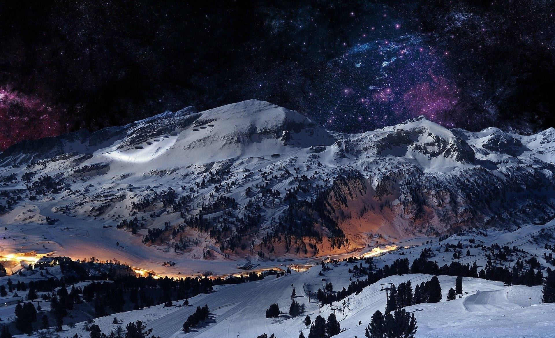 冬季 桌布 壁紙 — 積雪的山峰在充滿活力的星空下閃耀，伴隨著紫色星雲和遠處的山谷燈光。
