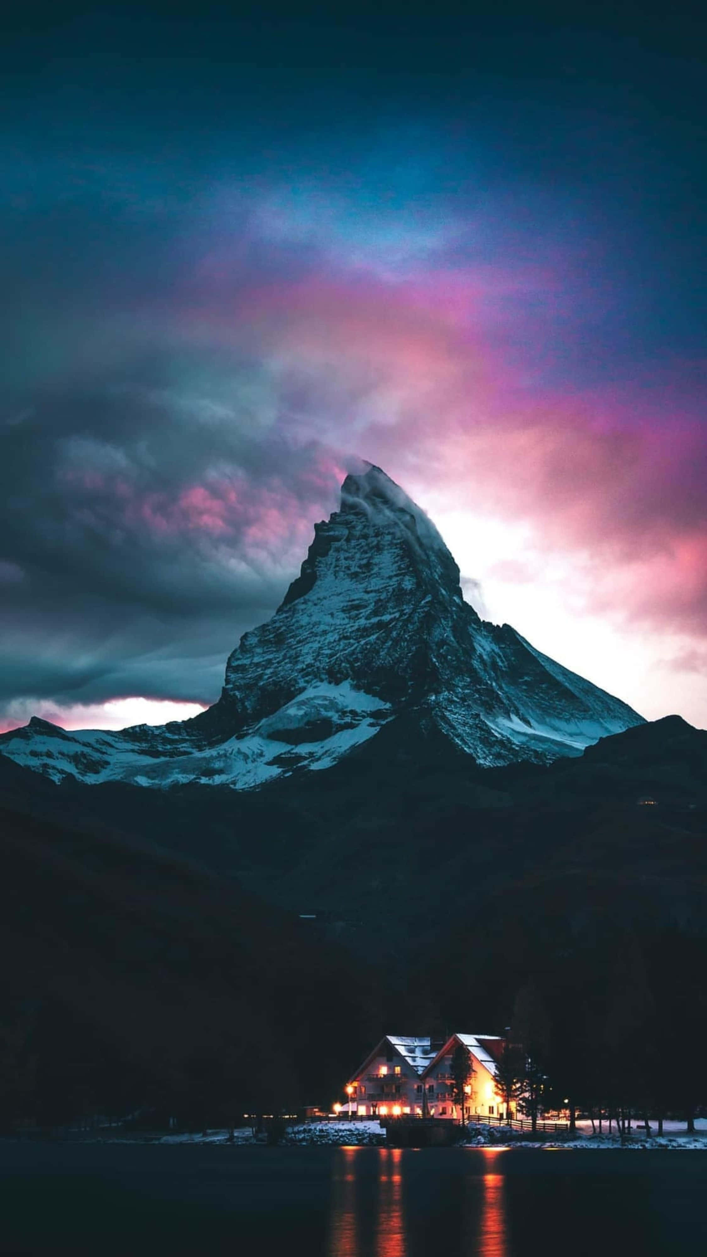 Nature Scenes 桌布 壁紙 — 積雪的山峰在充滿活力的暮色天空下升起，溫暖燈光的小屋倒映在下方平靜的湖面上。