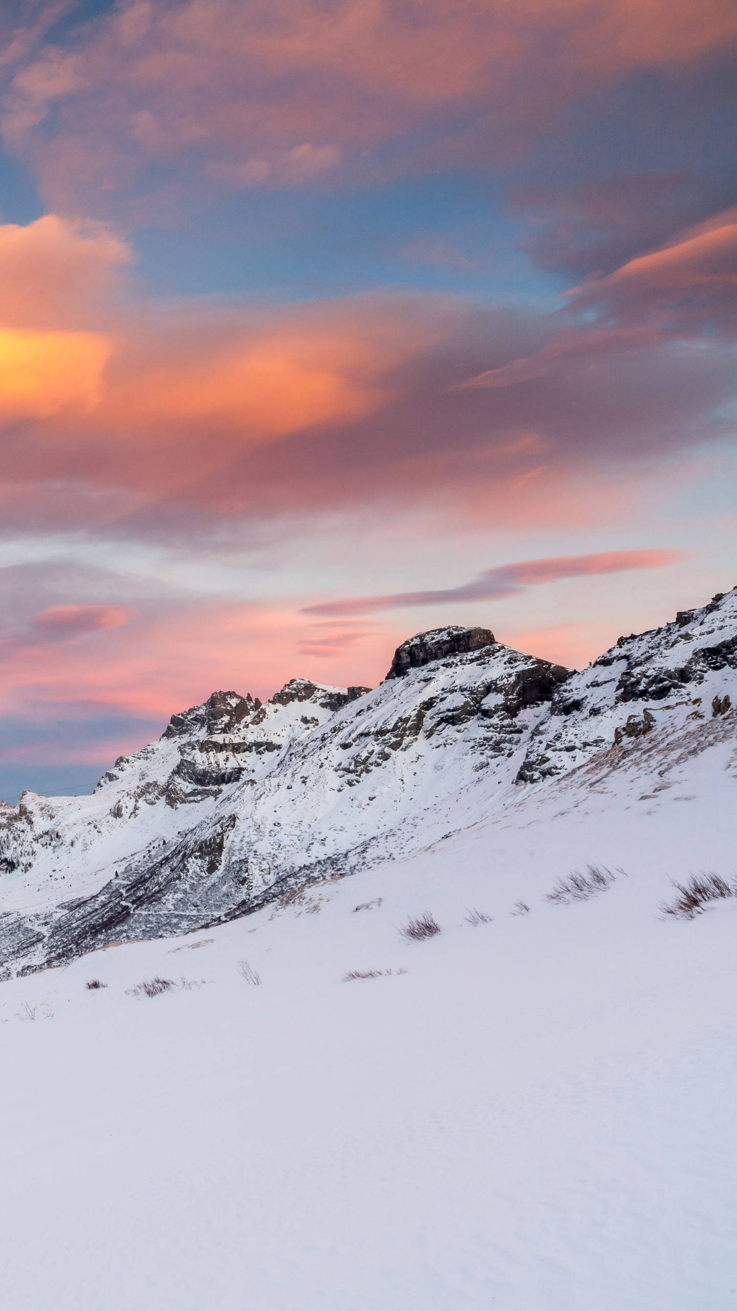 夕陽天空 桌布 壁紙 — 積雪的山峰在充滿活力的粉紅色和橙色日落天空下，伴隨著柔軟的雲朵。