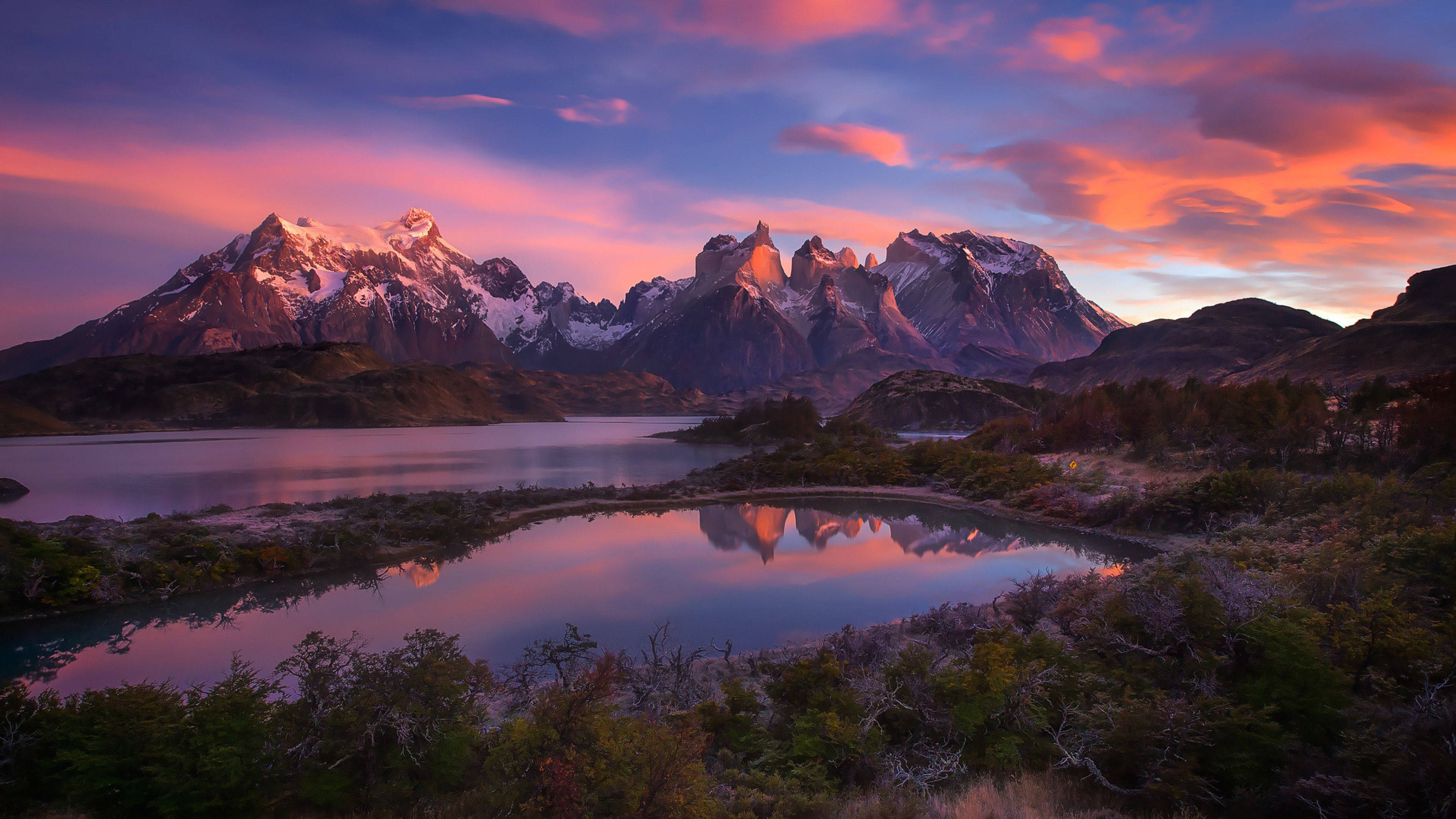 Patagonia 桌布 壁紙 — 積雪的山峰在充滿活力的粉紅色和紫色日落天空下，倒映在平靜的湖面上。