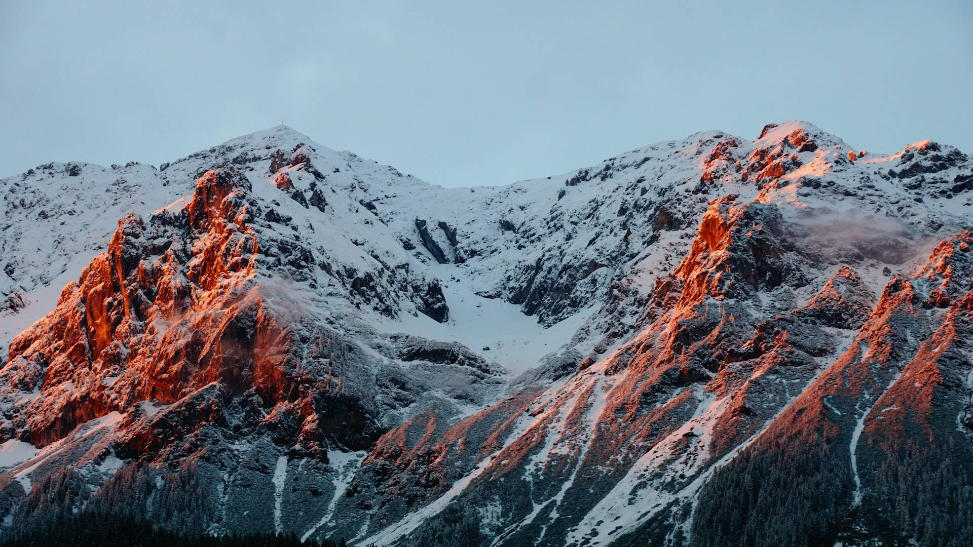 Mountain Landscape 桌布 壁紙 — 積雪的山峰在夕陽西下時散發出溫暖的橙色光芒，在崎嶇的地形上投下長長的陰影。
