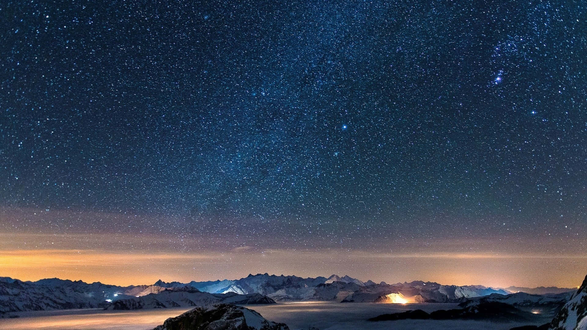 夜空 桌布 壁紙 — 積雪的山峰在廣闊的星空下閃耀，地平線散發溫暖的光芒。