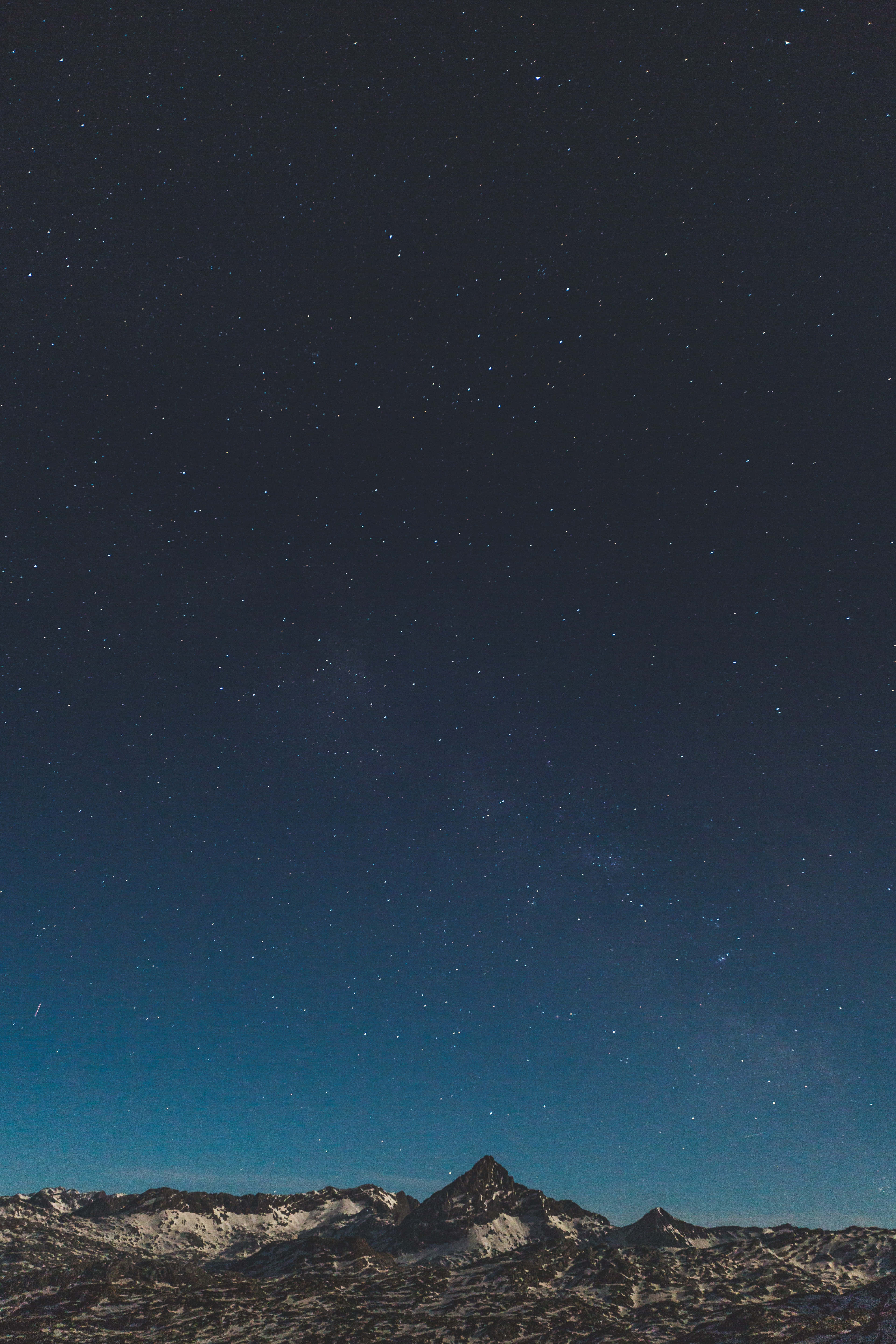 極簡 iPhone 桌布 壁紙 — 積雪的山峰在廣闊的星空夜空下聳立，散發著宇宙藍和深靛藍色調。