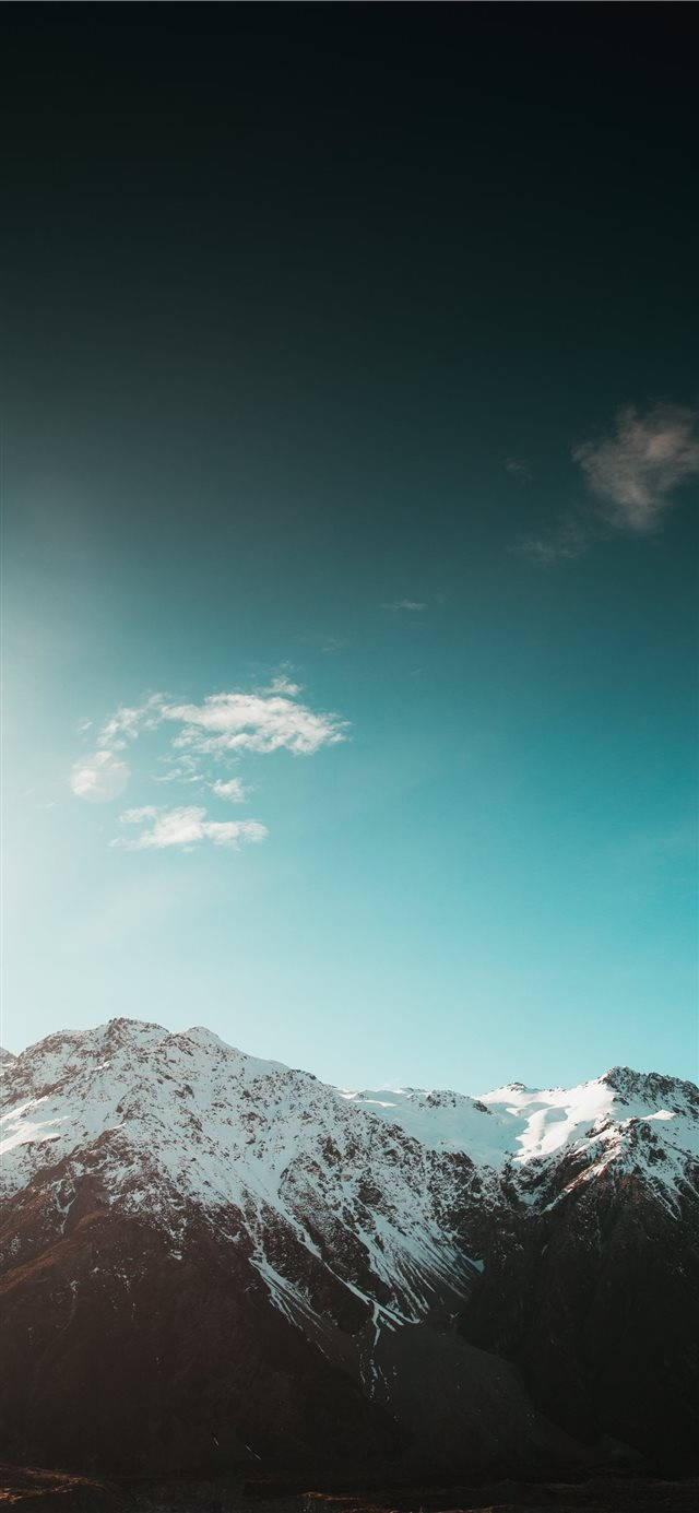  壁紙 — 積雪的山峰在廣闊的藍綠色天空和零星雲朵下聳立。
