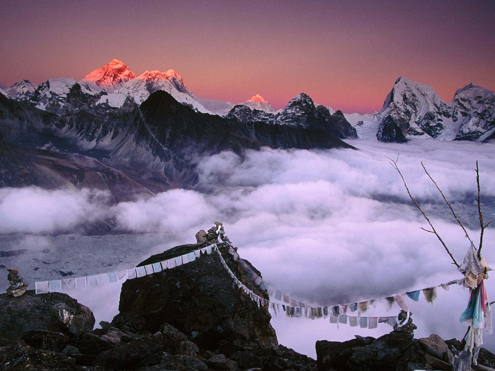 Mount Everest 桌布 壁紙 — 積雪的山峰在日出時呈現粉紅色光芒，雲海之上，岩石間掛著經幡。