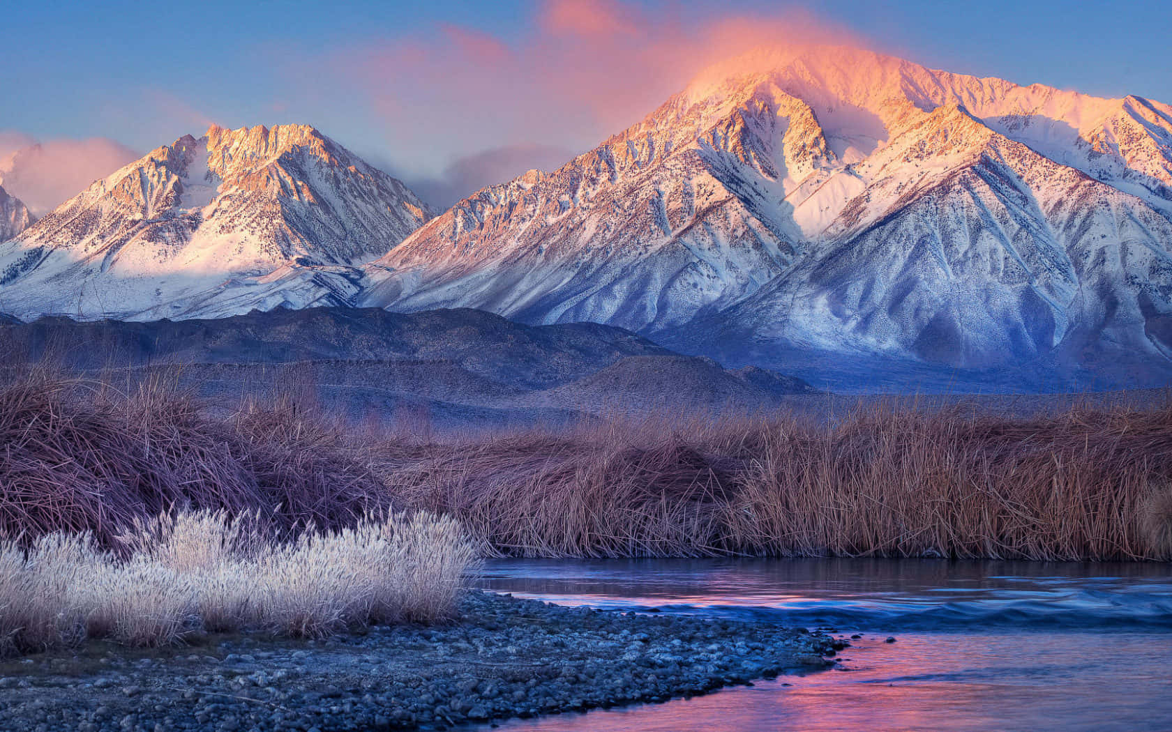 Snowy Mountain 桌布 壁紙 — 積雪的山峰在日出時閃耀著粉紅色和金色，河流在結霜的蘆葦下倒映著天空。
