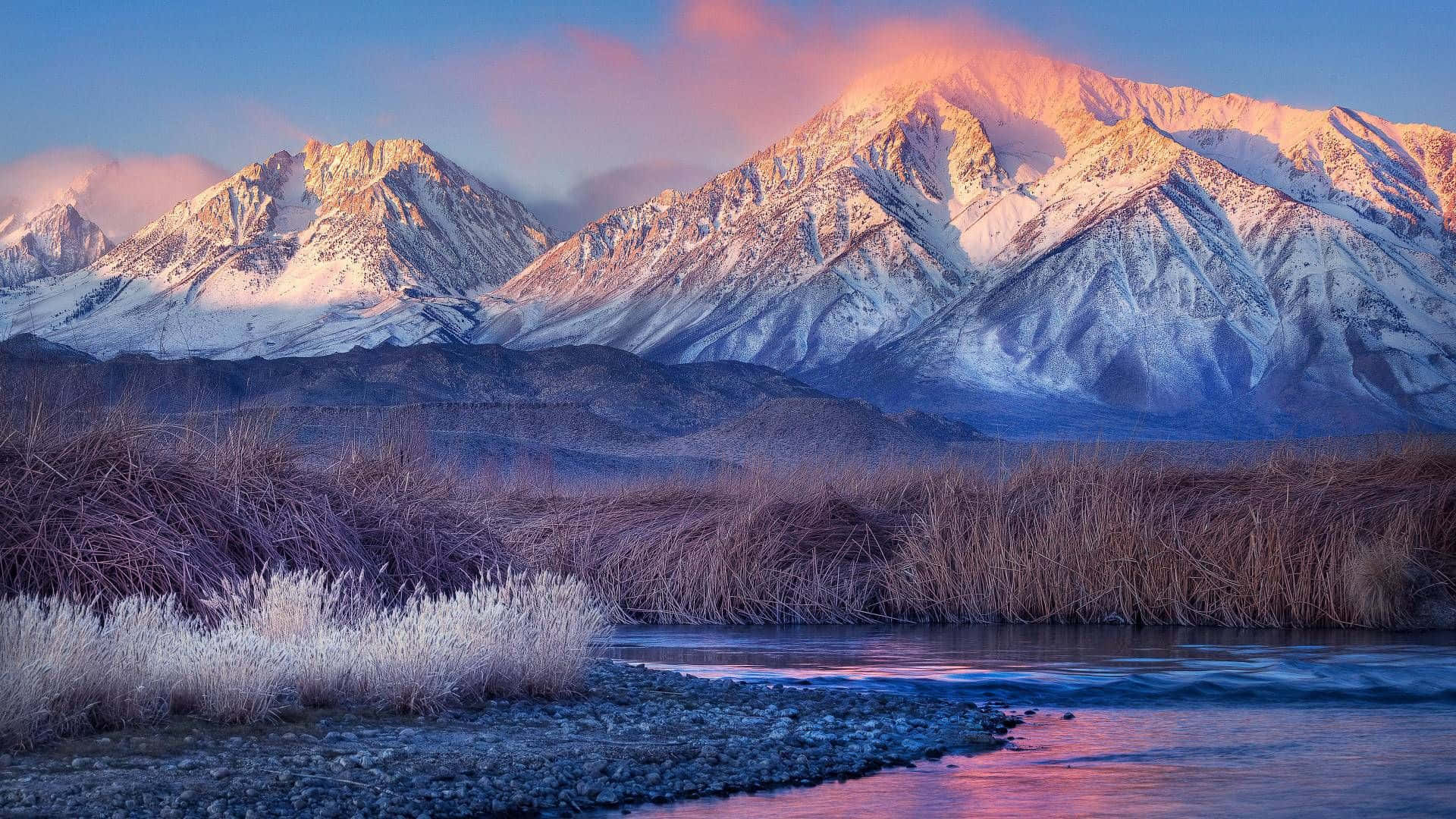 Mountain Scenes 桌布 壁紙 — 積雪的山峰在日出時閃耀著粉紅色和金色，河流在結霜的蘆葦下倒映著天空。
