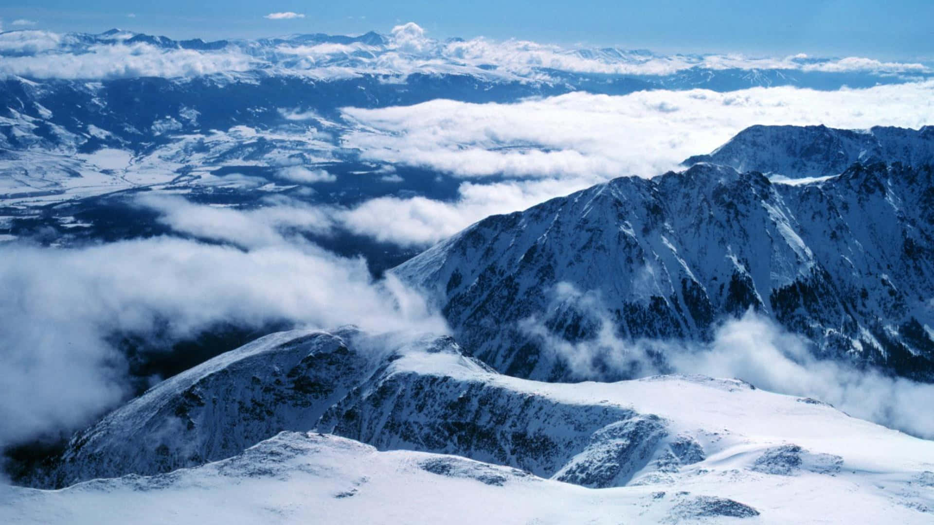  壁紙 — 積雪的山峰在晴朗的藍天下穿過雲海。