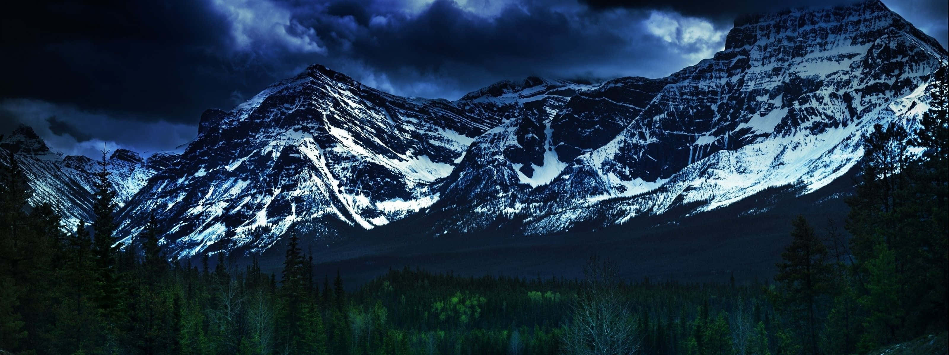 Mountain Range 桌布 壁紙 — 積雪的山峰在暴風雨夜空中聳立於黑暗森林之上。