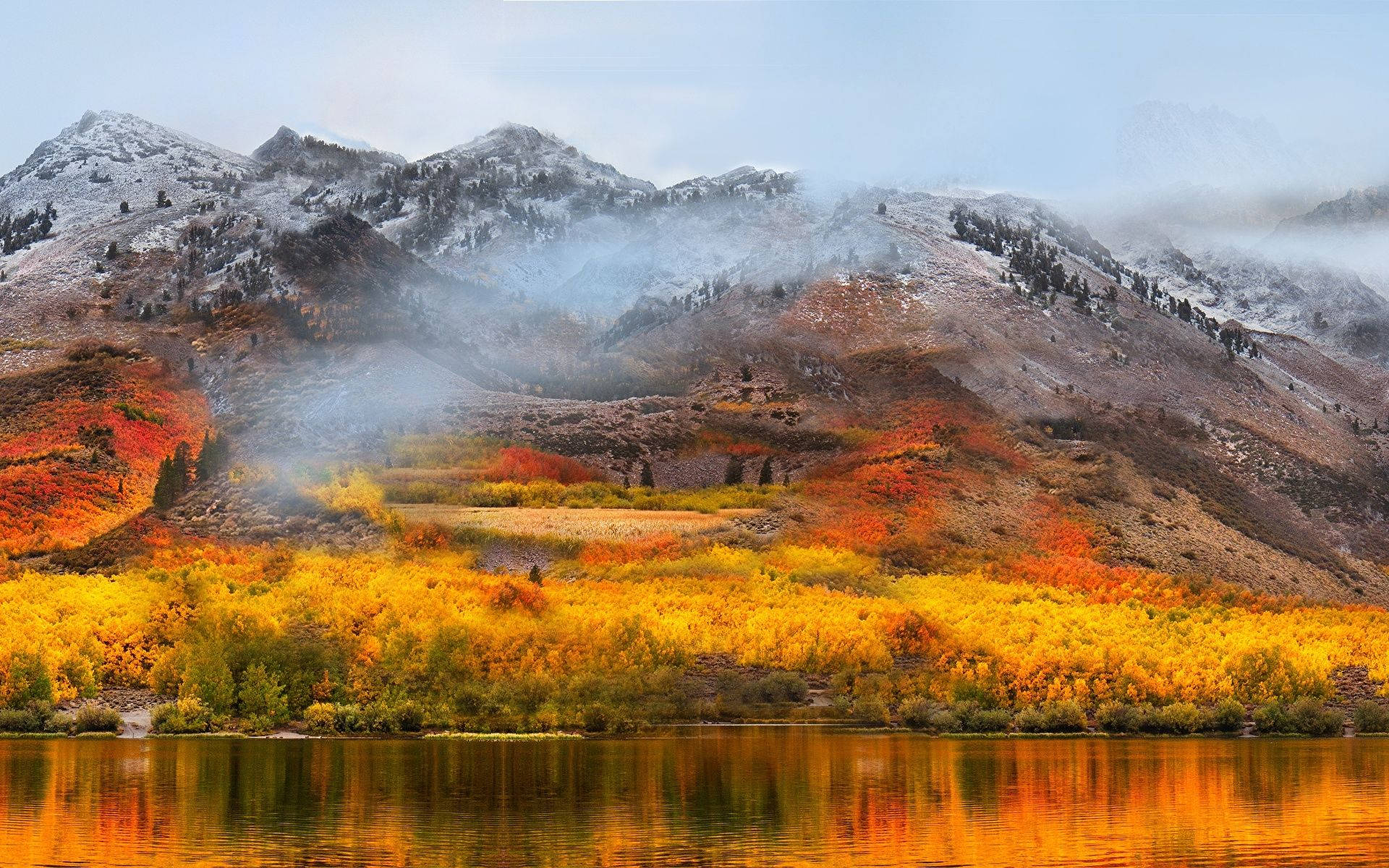macOS 桌布 壁紙 — 積雪的山峰在柔和日光下，聳立於倒映在平靜湖面上的 vibrant 秋林之後。