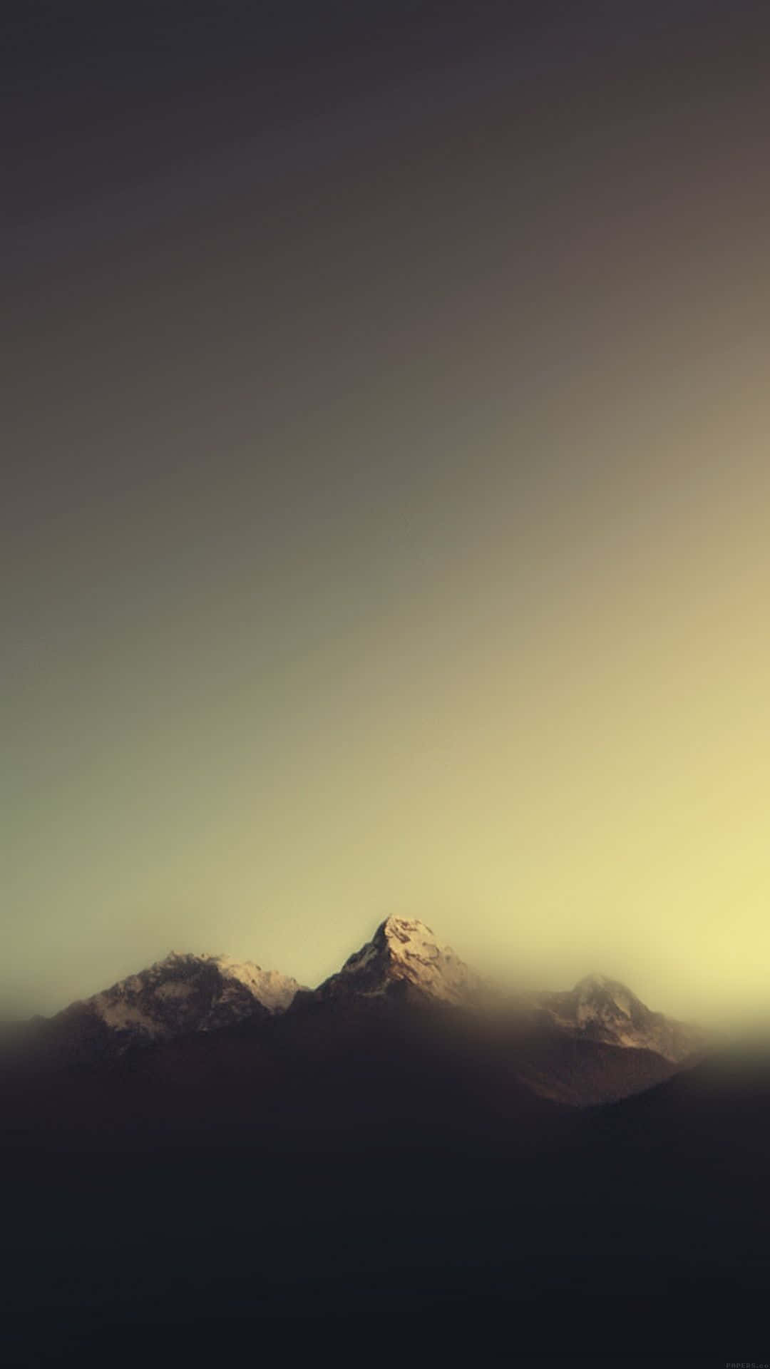 極簡 iPhone 桌布 壁紙 — 積雪的山峰在漸變的天空下從薄霧中浮現，天空閃耀著溫暖的日落色調。