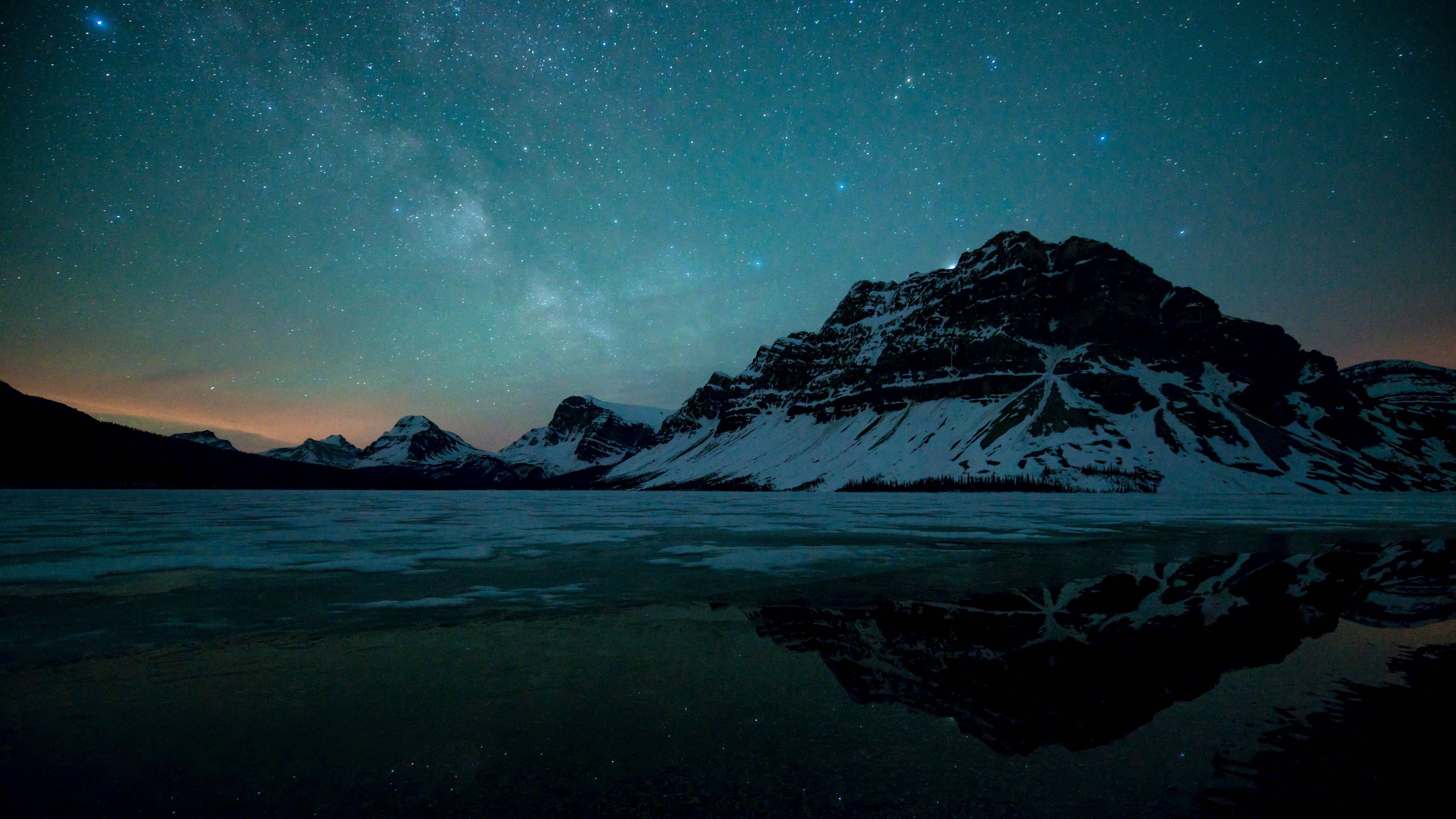 MacBook Pro 4K 桌布 壁紙 — 積雪的山峰在繁星點點的夜空下倒映，銀河在冰凍的湖面上拱起。