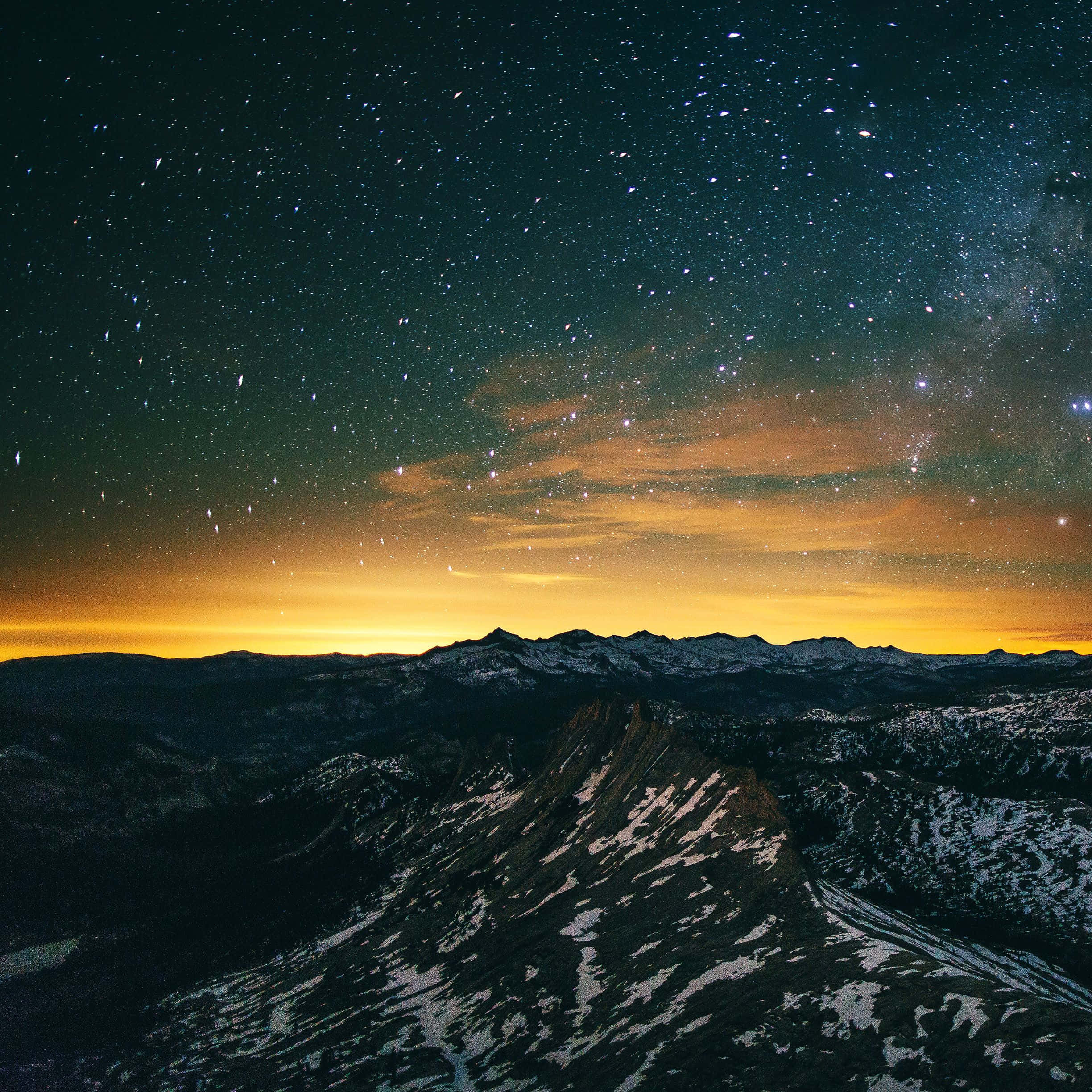 iPad Pro 桌布 壁紙 — 積雪的山峰在繁星點點的夜空下升起，夜空閃爍著橙色的極光雲。