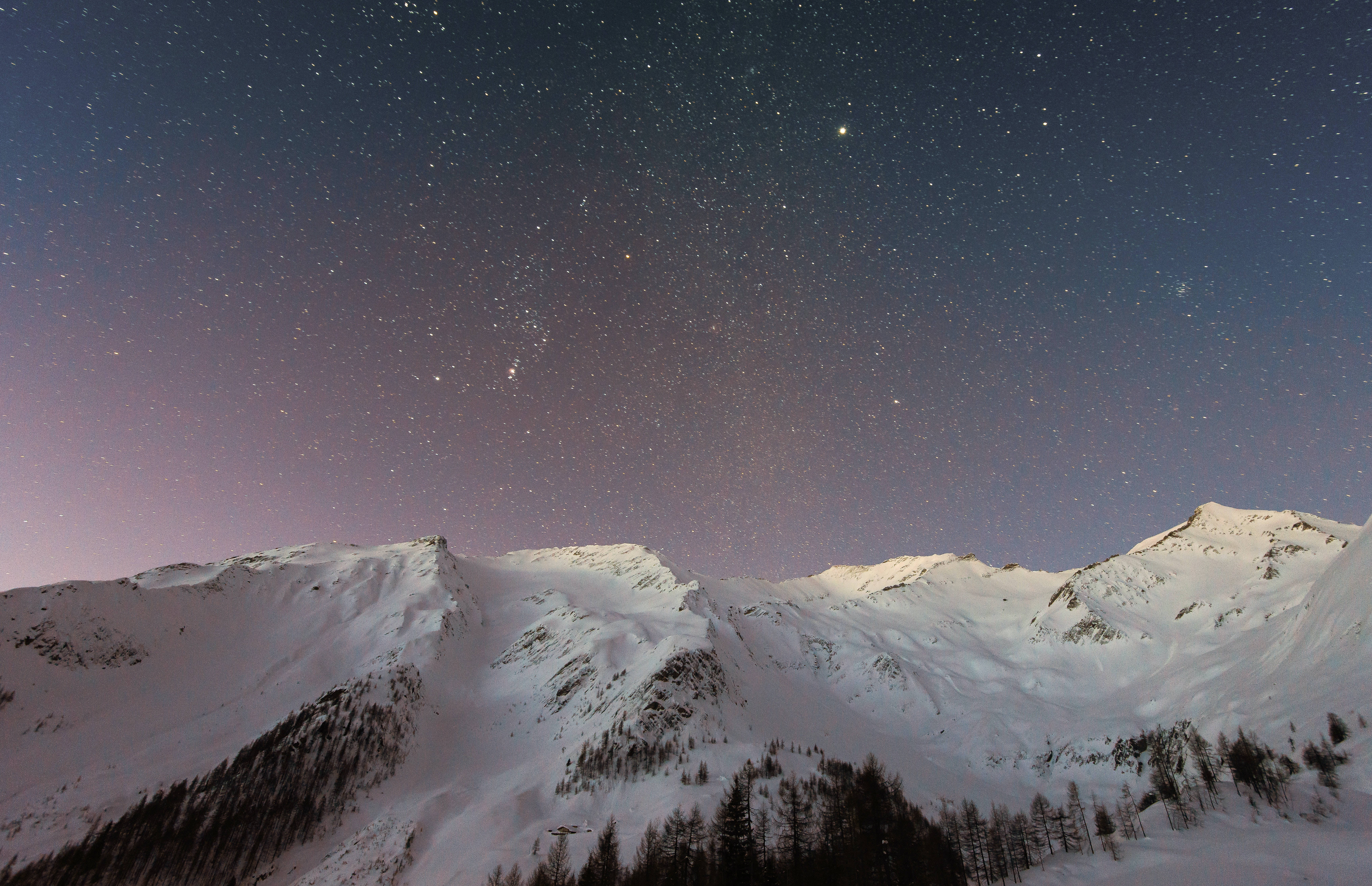 iPhone 桌布 壁紙 — 積雪的山峰在閃爍著柔和紫色極光的星空夜空下聳立。