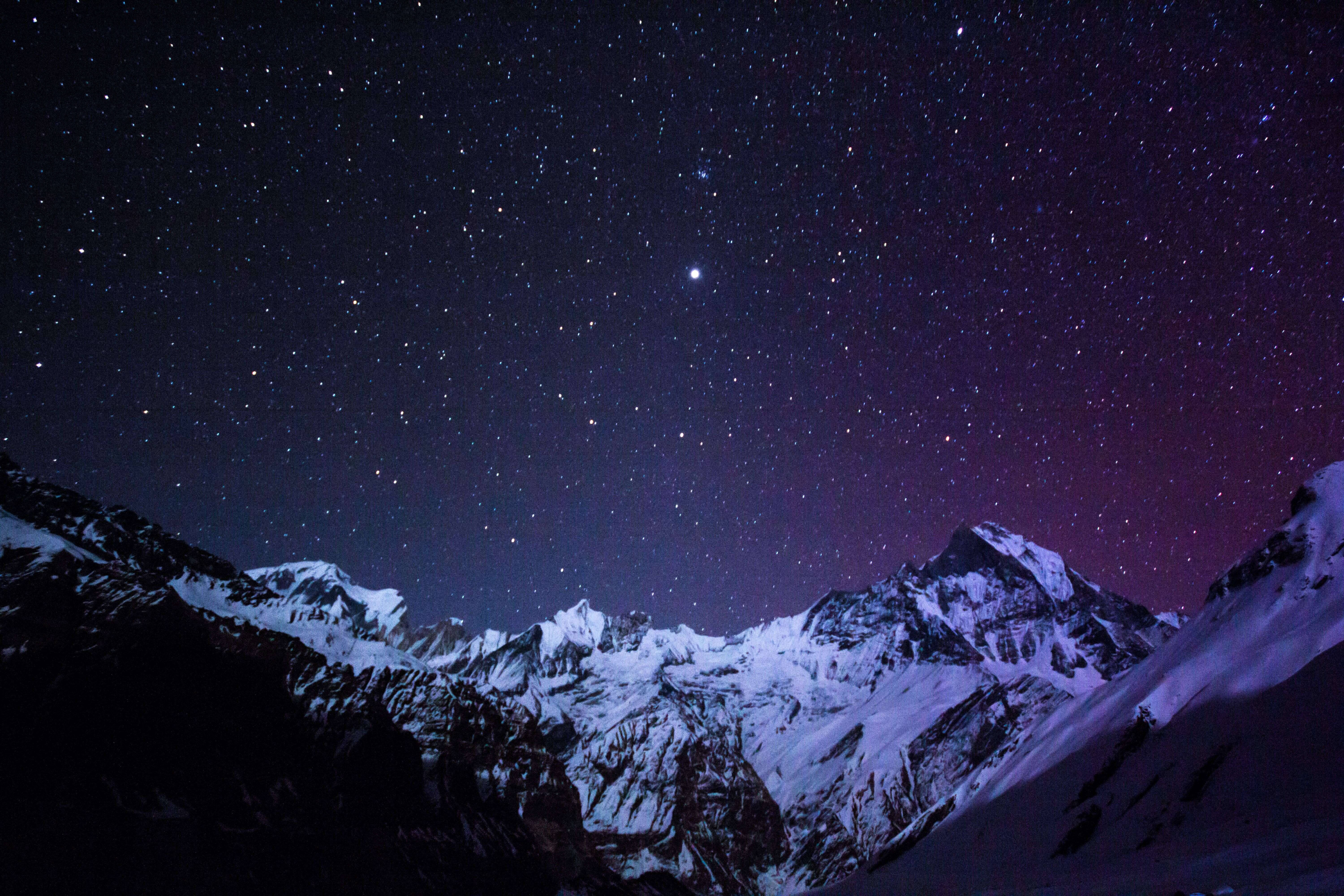 自然 4K 桌布 壁紙 — 積雪的山峰在閃爍著紫色極光的星空下聳立。