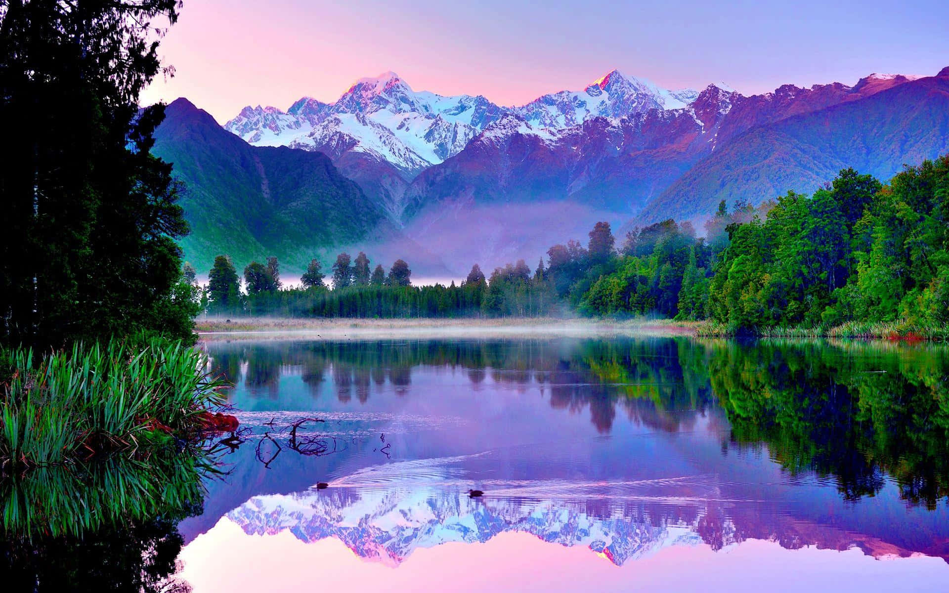 Lake 桌布 壁紙 — 積雪的山峰在黎明時分倒映在霧氣瀰漫的湖中，天空呈現鮮豔的粉紅色和紫色。