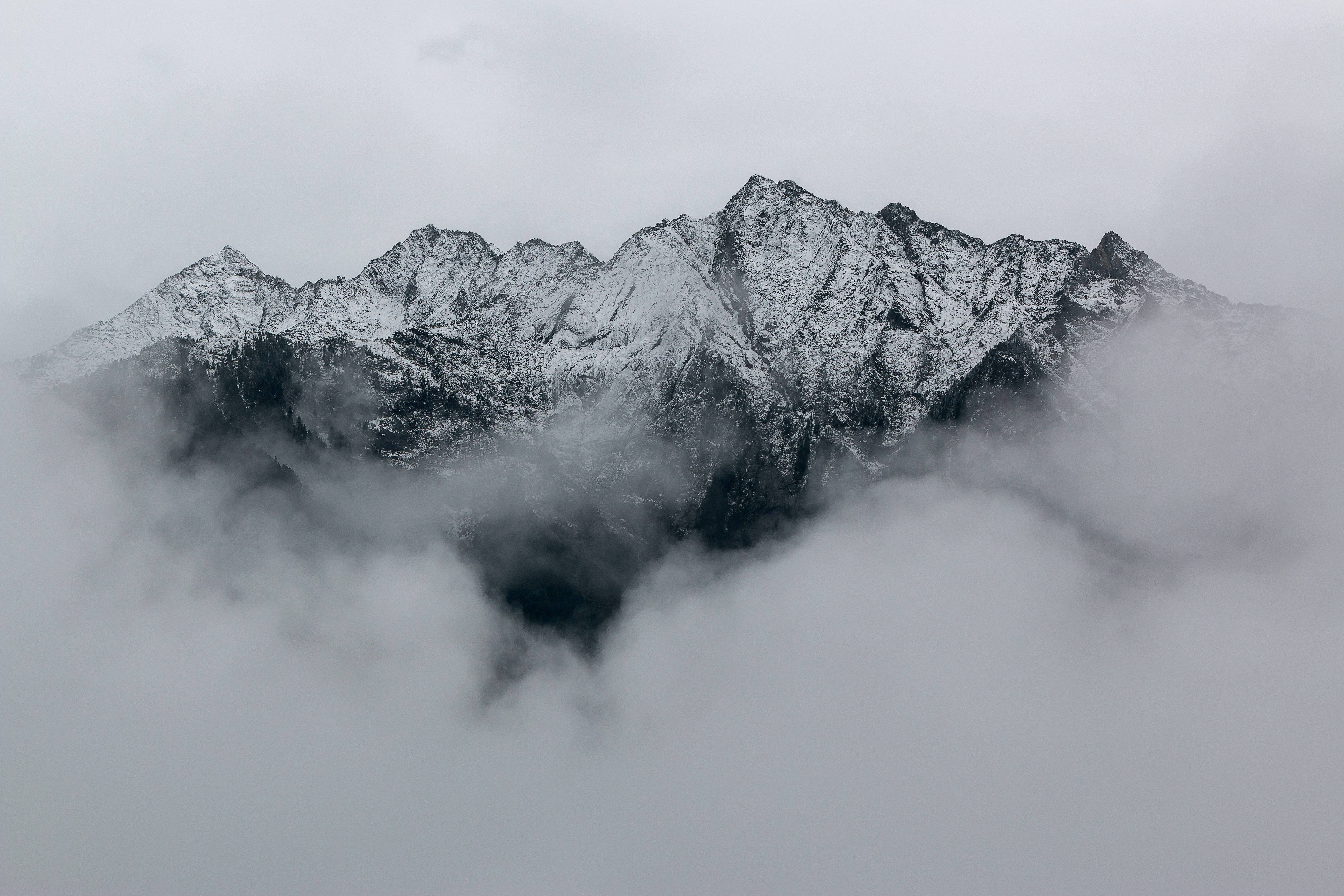 Mountain Landscape 桌布 壁紙 — 積雪的山峰穿過濃霧，在陰天之下營造出寧靜而神秘的高山景象。