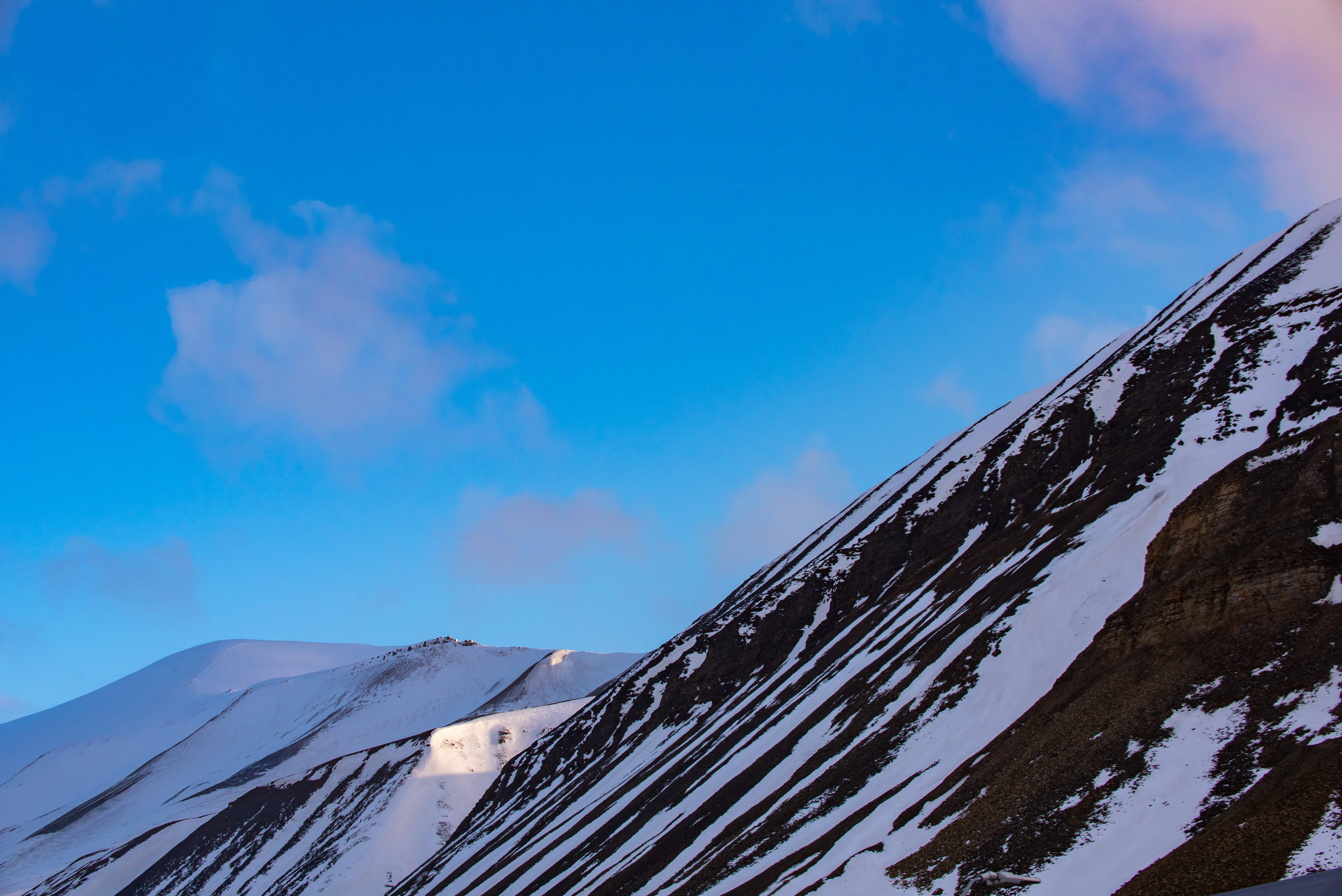 Svalbard 桌布 壁紙 — 積雪的山脊沐浴在金色的日出光芒中，映襯著帶有縷縷雲彩的鮮豔藍天。