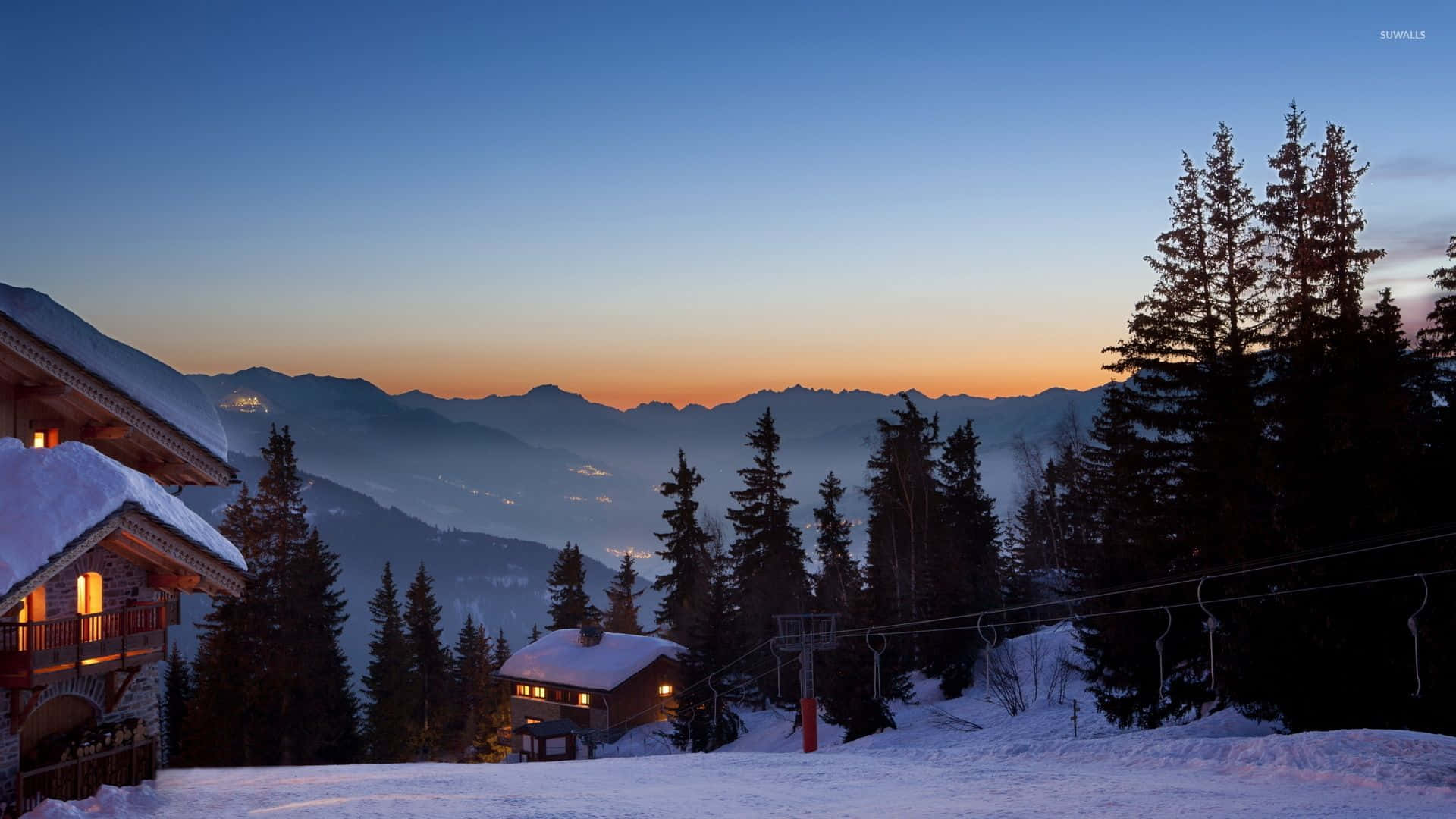 Ski Resort 桌布 壁紙 — 積雪的山間小木屋在黃昏時散發溫暖光芒，映襯著漸變天空、遠山和常青樹。