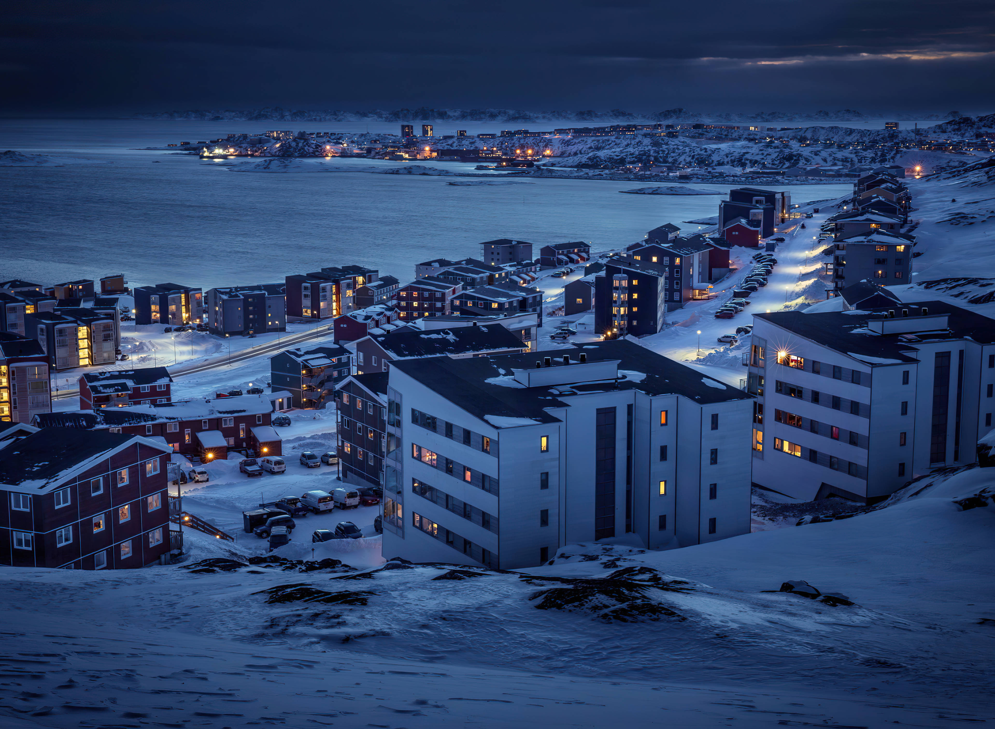 Greenland 桌布 壁紙 — 積雪的建築物在俯瞰冰封海洋的黑暗冬日天空中溫暖地發光。