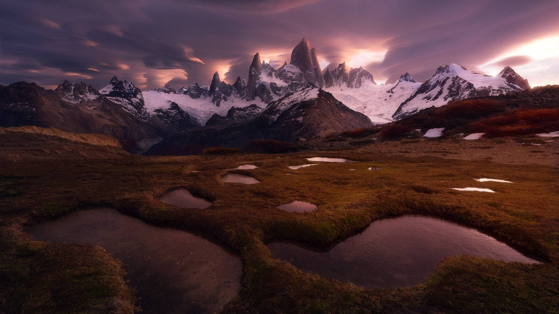 Chile 桌布 壁紙 — 積雪覆蓋的鋸齒狀山峰在戲劇性的紫色日落中升起，將溫暖的光線投射在反射池和金色草原上。