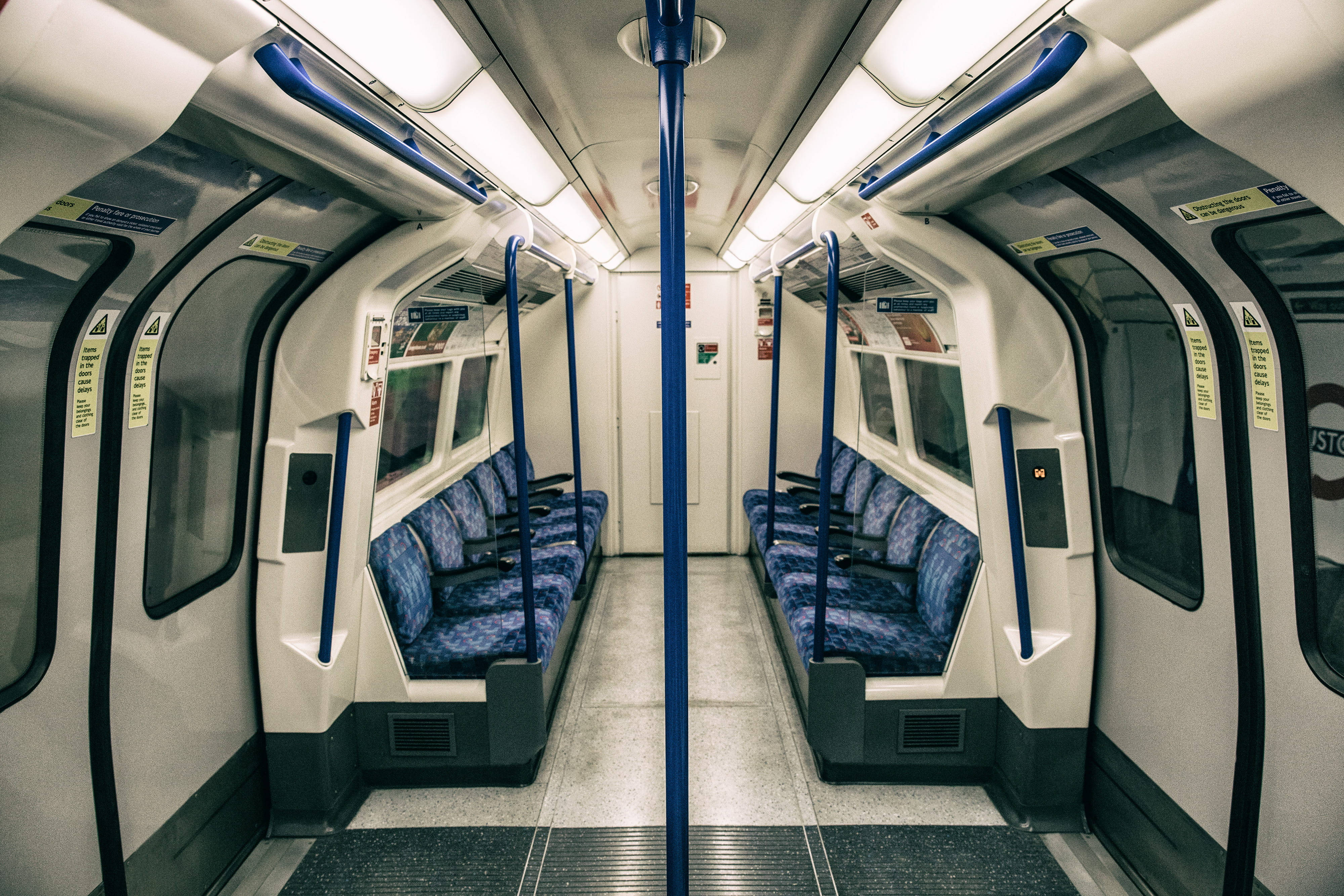 Subway 桌布 壁紙 — 空曠的地鐵車廂內部，配有藍色圖案座椅和頭頂扶手，在明亮的螢光燈下。