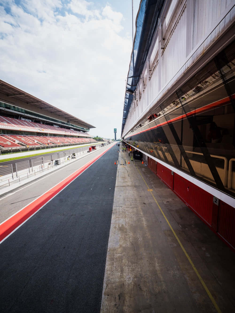 Race Track 桌布 壁紙 — 空曠賽道的廣角視角，設有紅色看台和維修區建築，天空部分多雲。