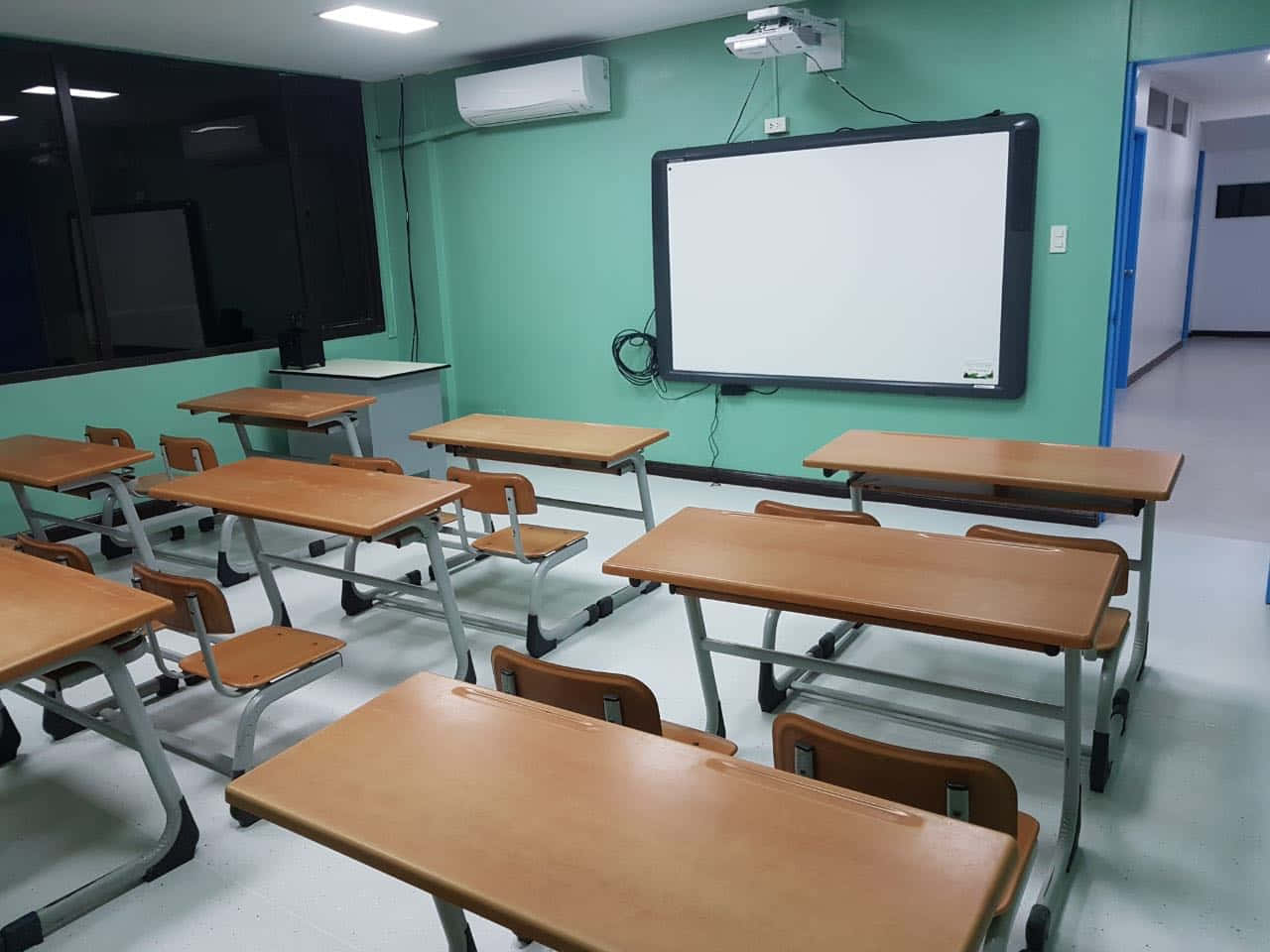 Real Classroom 桌布 壁紙 — 空無一人的教室，有木製書桌、椅子，以及螢光燈下的大型白板。