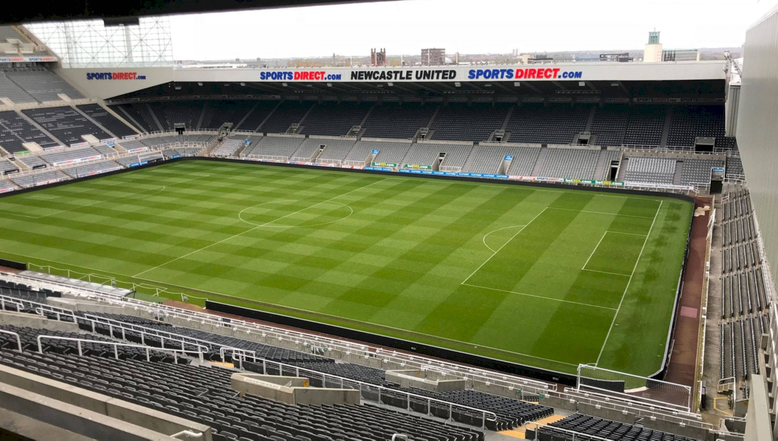 Football Field 桌布 壁紙 — 空無一人的足球場鳥瞰圖，翠綠的草地和灰色的座位在陰天之下。