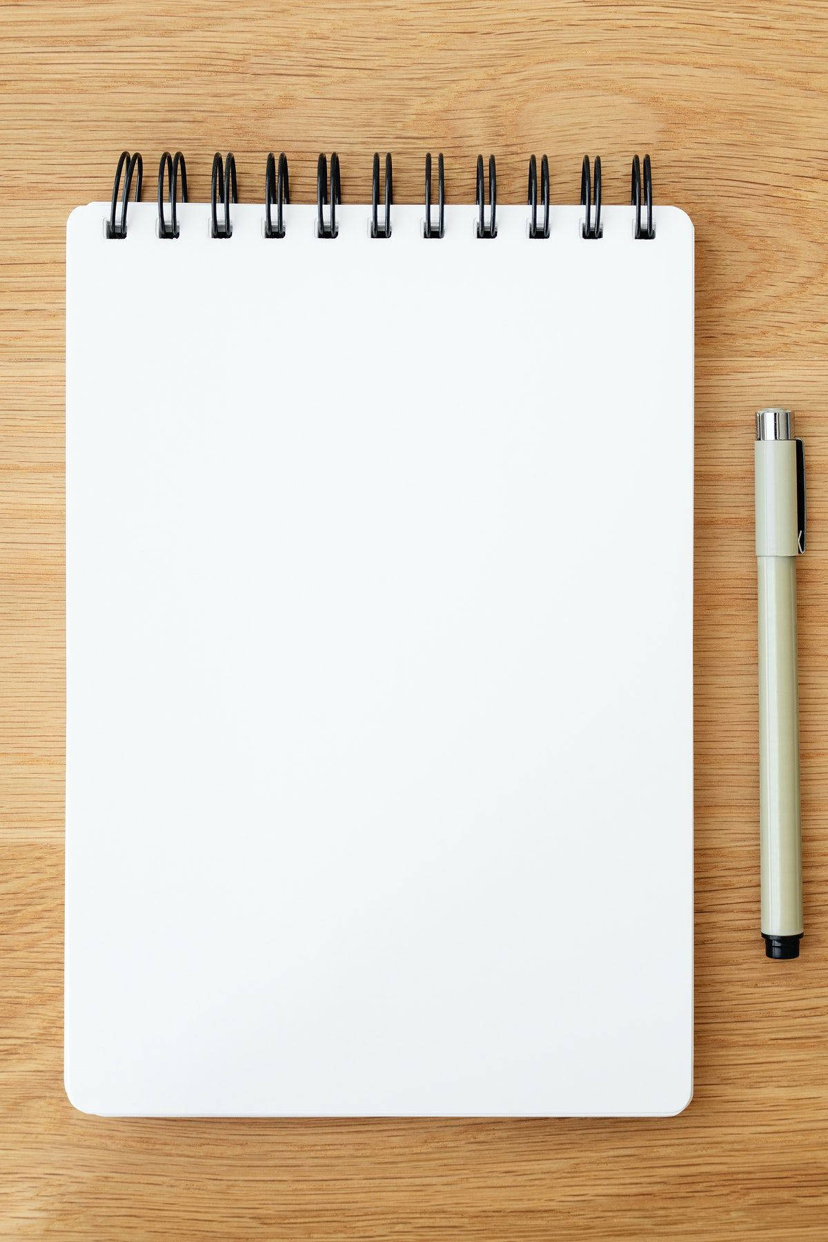 paper 桌布 壁紙 — 空白白色螺旋筆記本和米色筆放在溫暖的木質表面上，準備好進行創意使用。