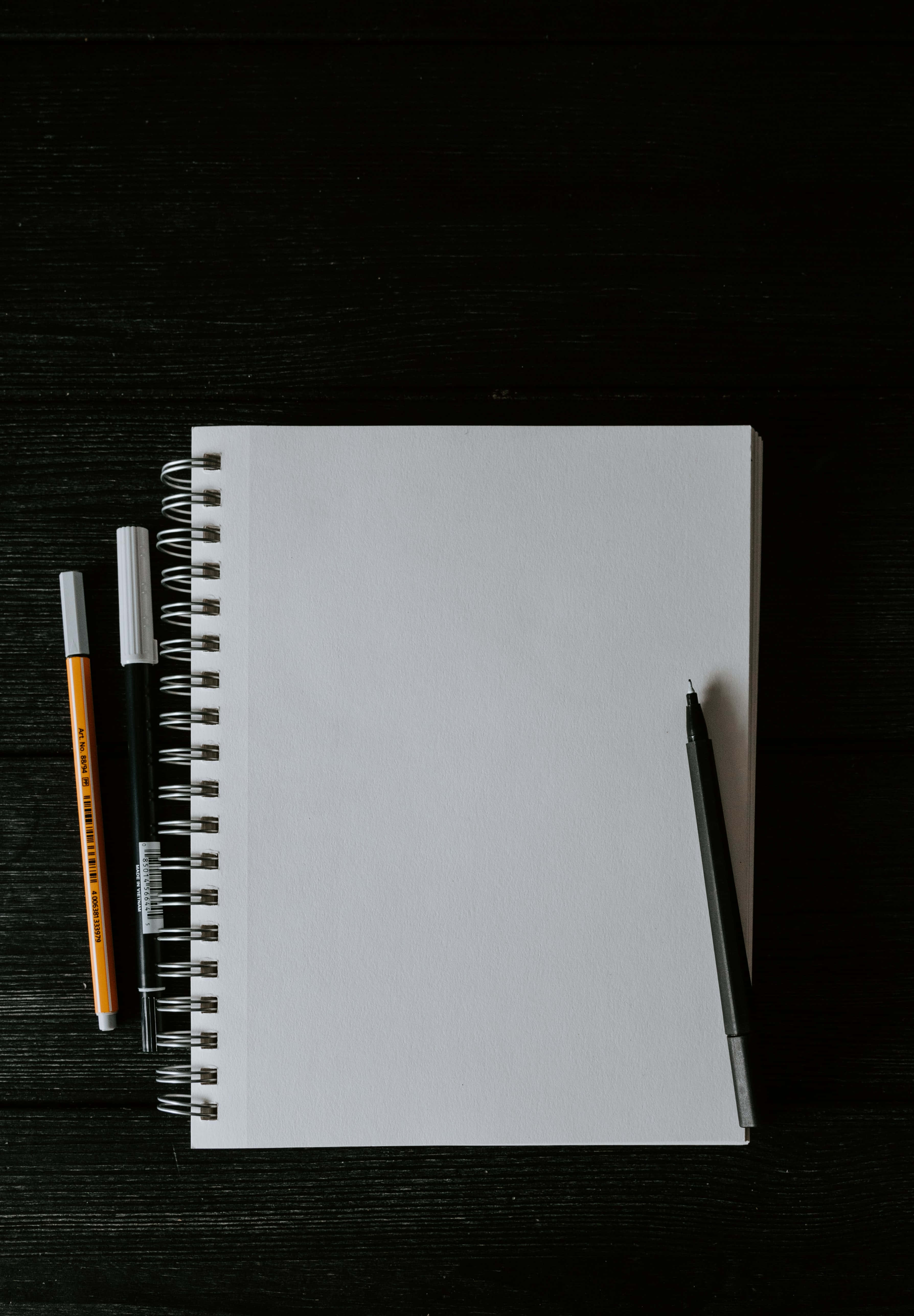 Notebook 桌布 壁紙 — 空白螺旋筆記本與筆放置在深色木質表面上，極簡俯拍。